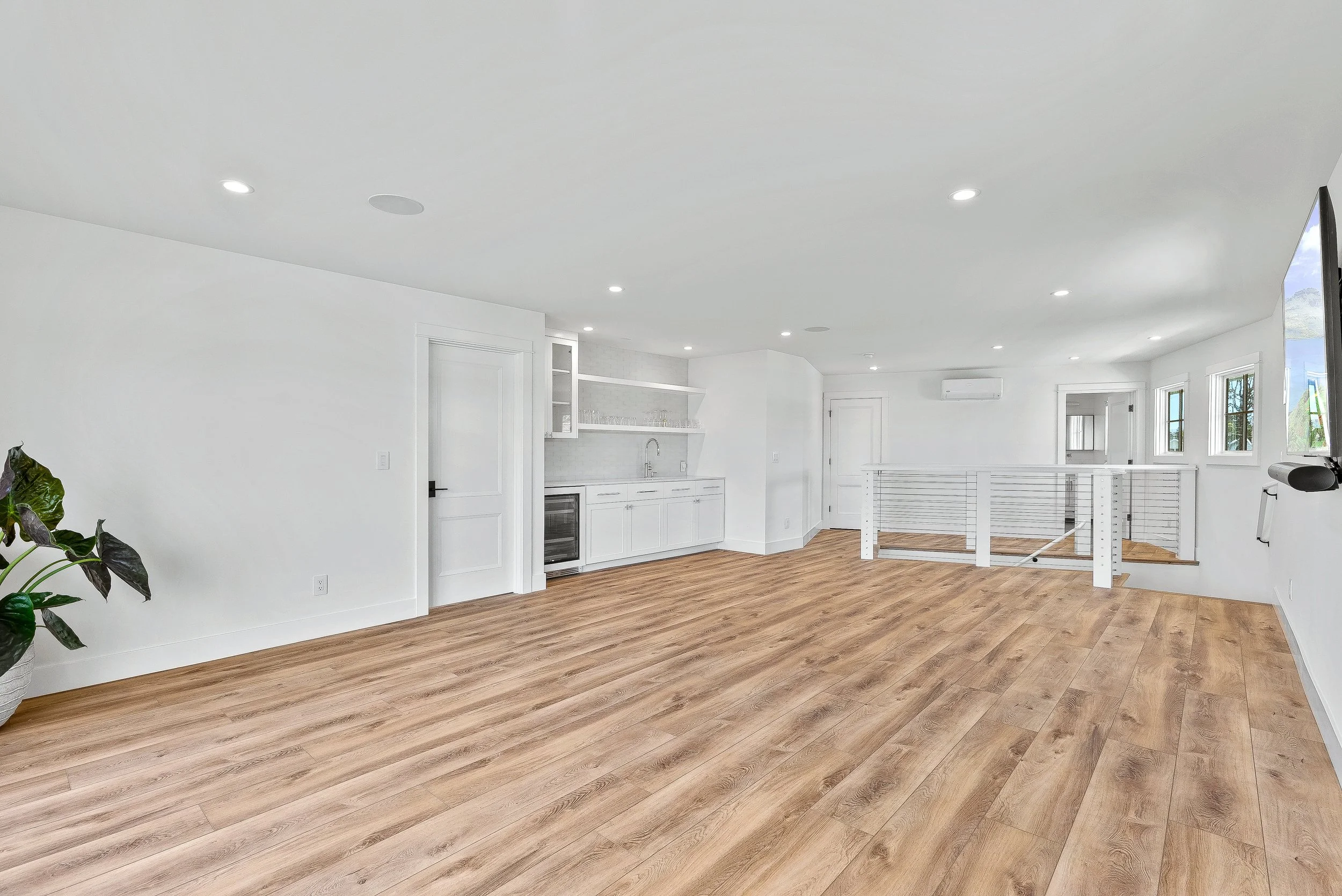 Empty living space with white walls, hardwood flooring, and built-in kitchenette, featuring windows and a safety railing in Capitola, California.