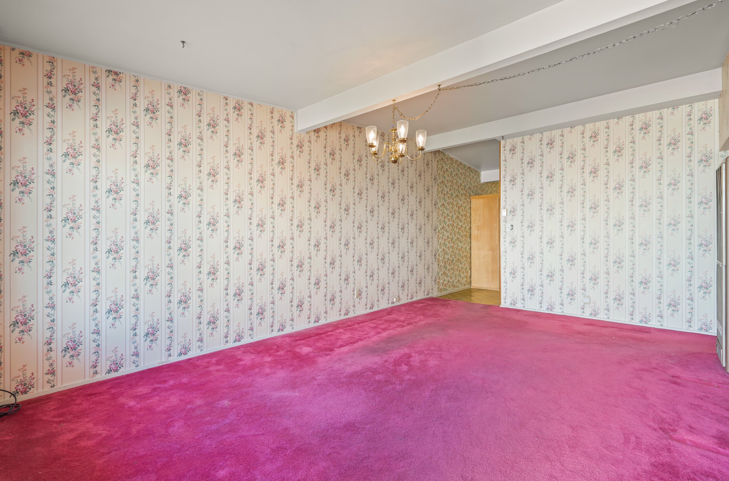 Empty living room with floral wallpaper and pink carpet, hanging chandelier, and some wall detailing in Salinas, Monterey county, CA.