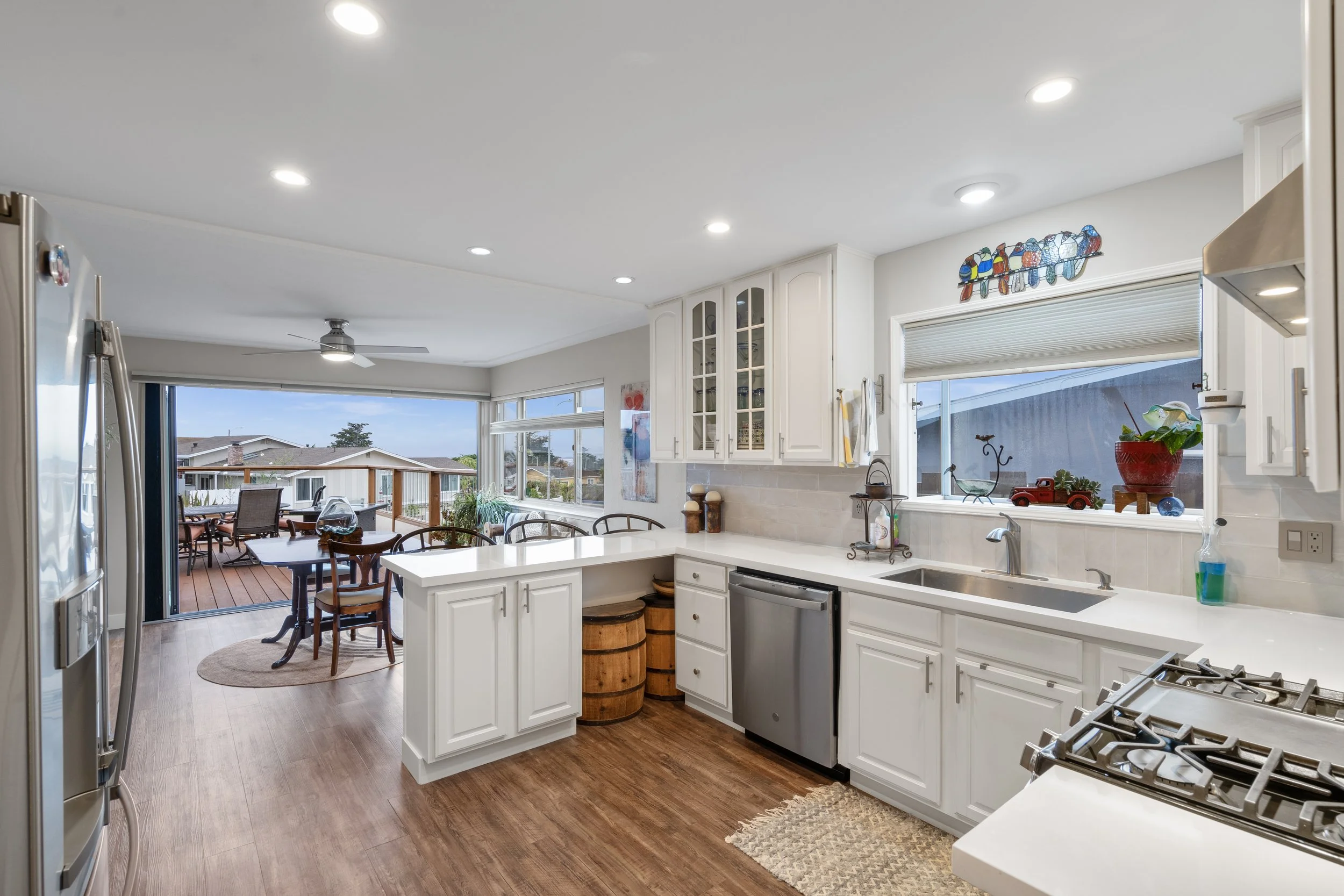 Kitchen with white cabinetry, stainless steel appliances, and a view of the dining area and outdoor deck through large windows.