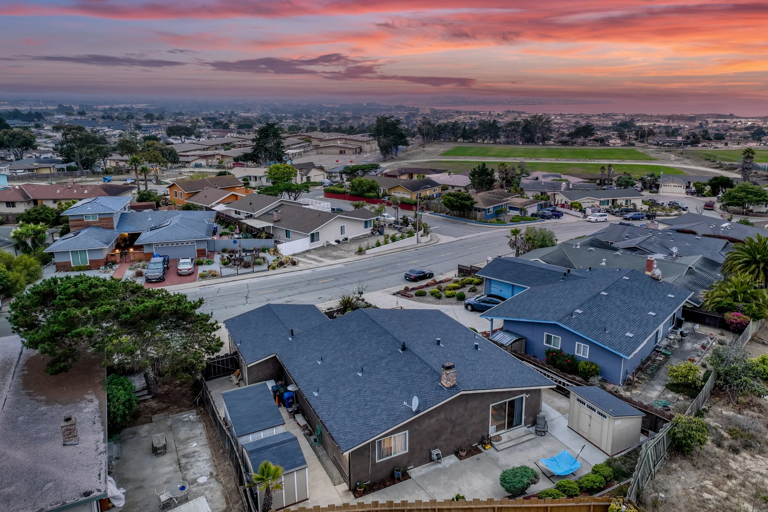 Aerial view of suburban neighborhood at sunset with various houses, trees, and a distant field in Seaside, California.