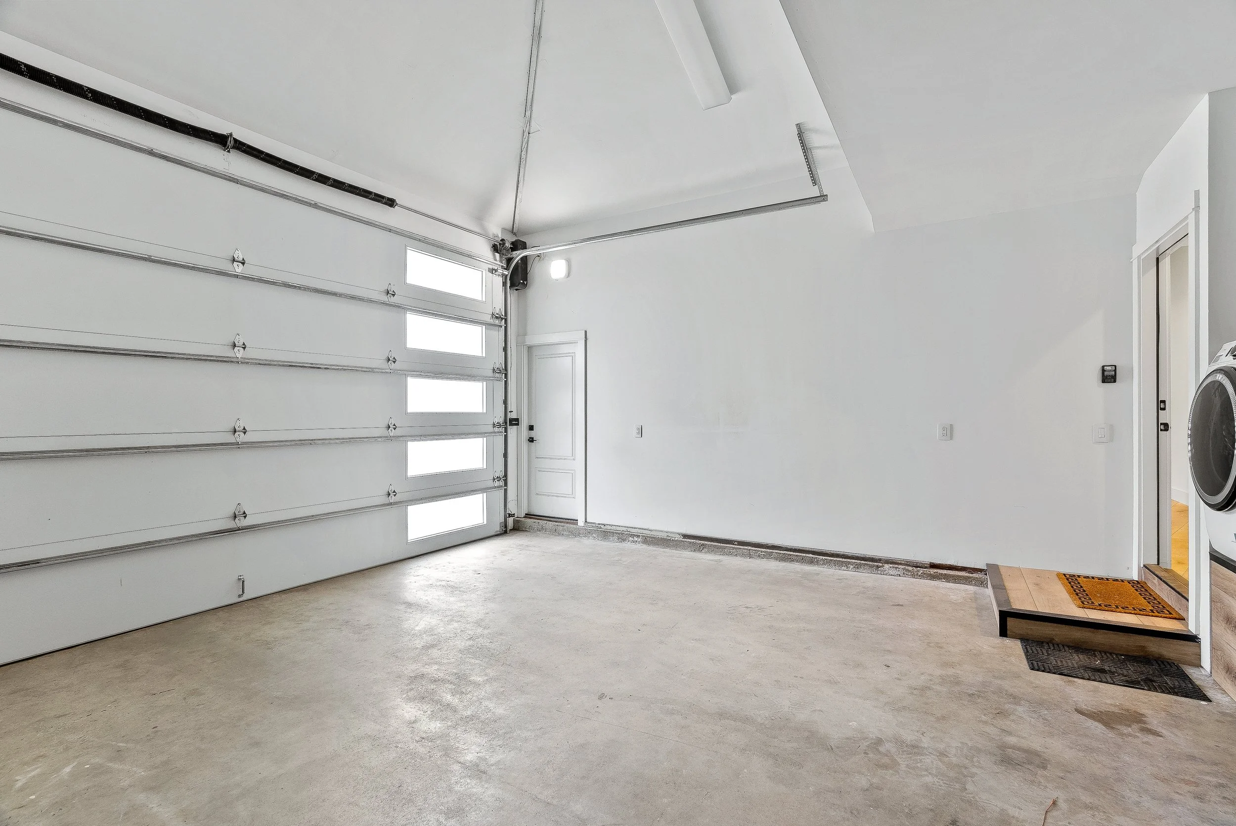 Empty garage with a closed white sectional garage door, a concrete floor, and a small laundry area with a washing machine in Capitola, California.
