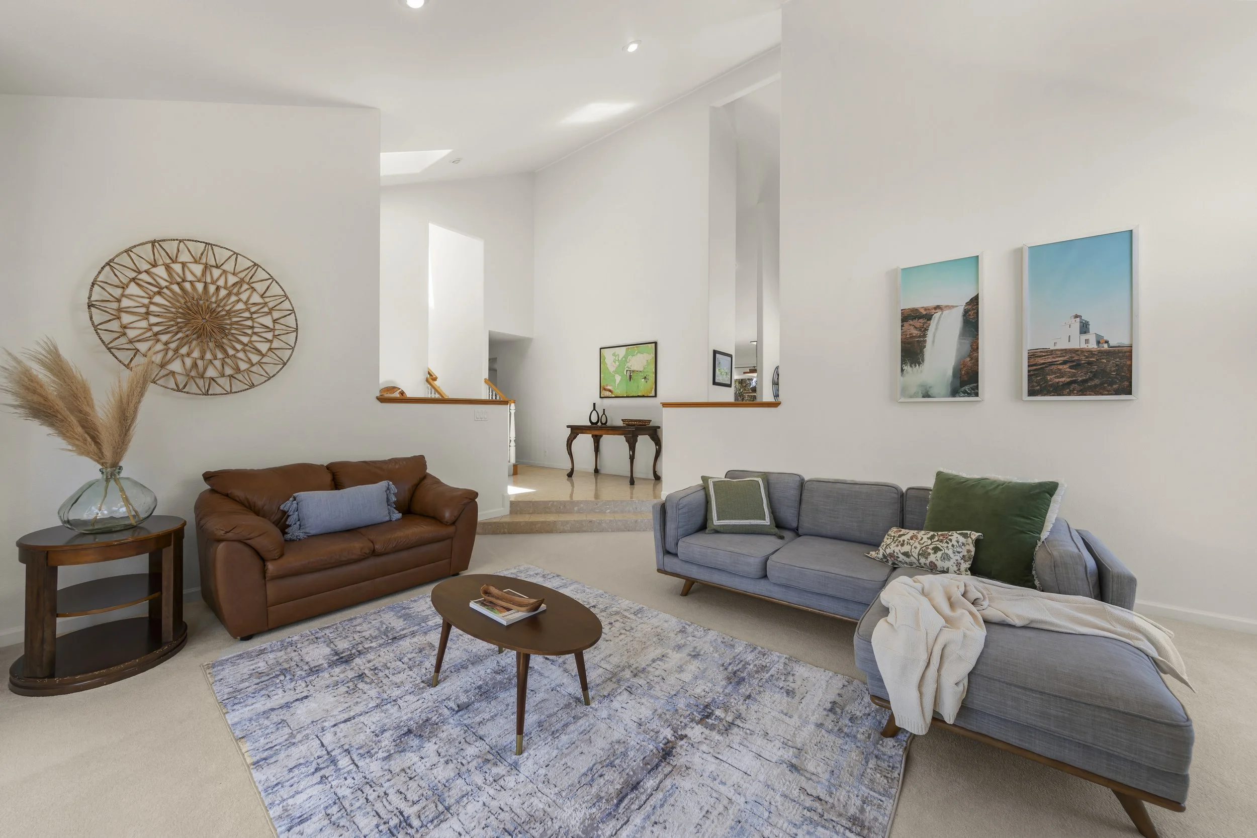 Living room with two sofas, a wooden coffee table, a decorative wall hanging, framed artwork on the walls, and a carpeted floor.