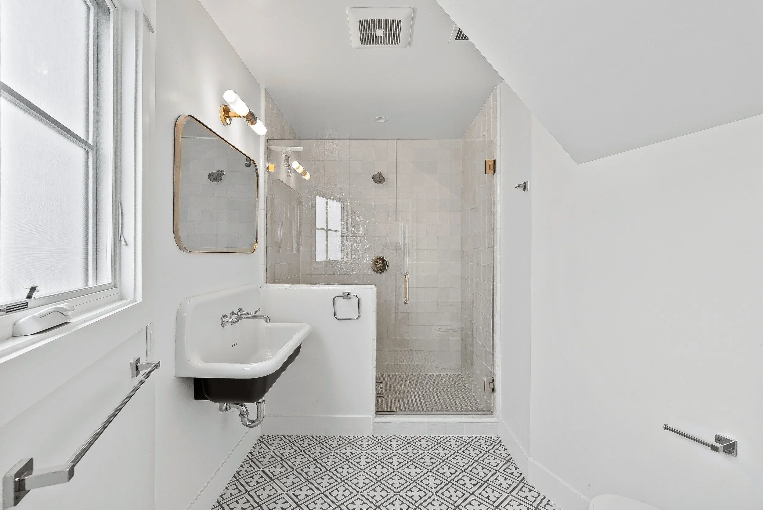 Bright bathroom with a glass shower, white sink, mirror, window, and patterned floor tiles in Capitola, California.