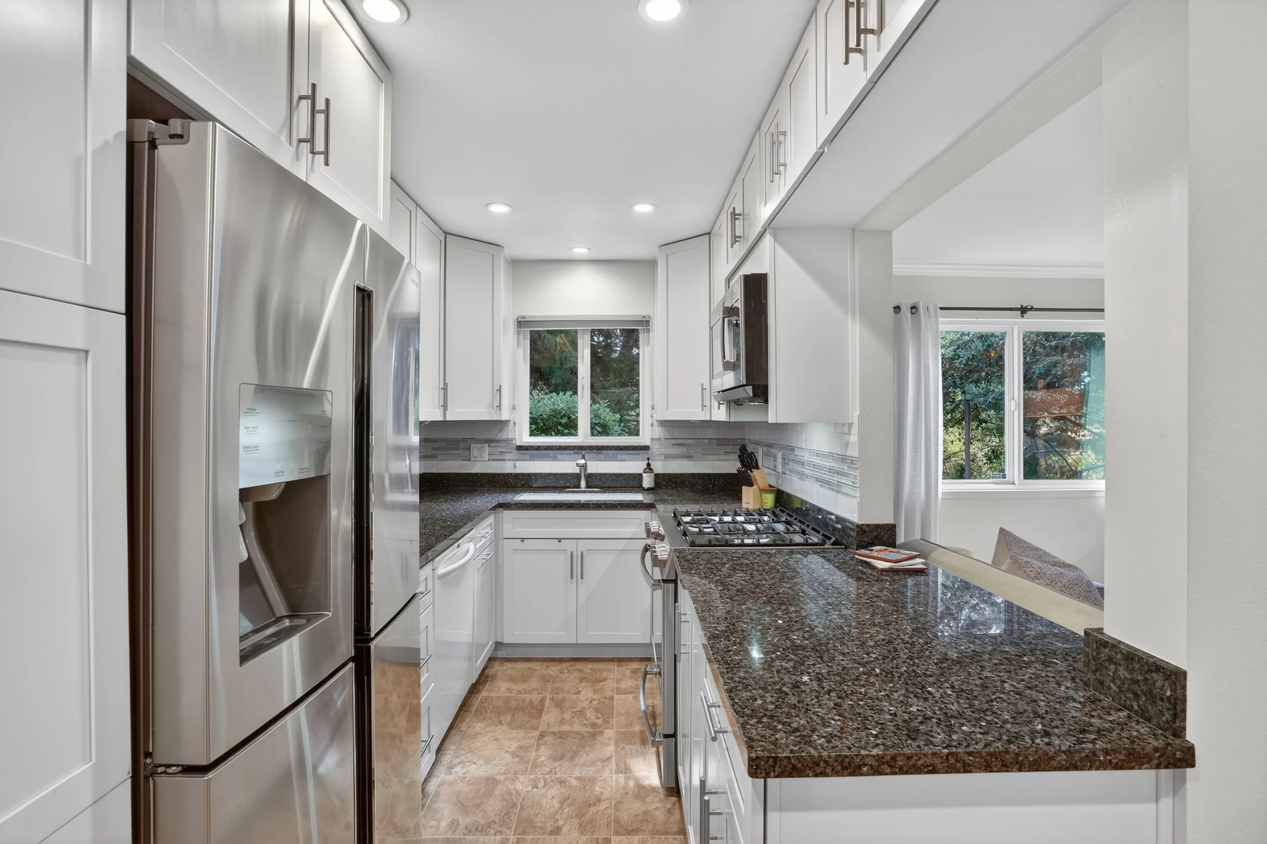 Modern kitchen with white cabinets, dark granite countertops, stainless steel appliances, and a window above the sink.