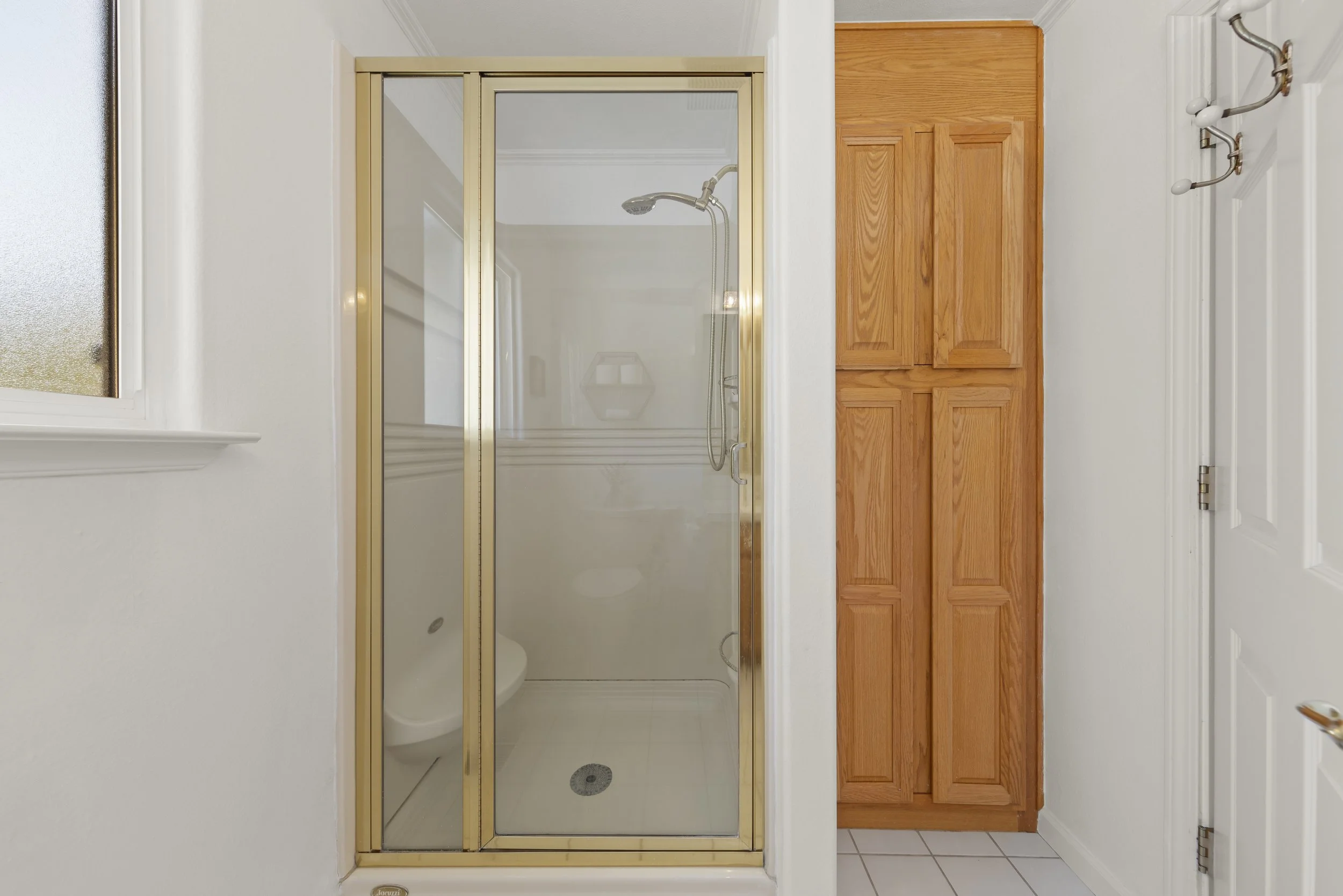 Bathroom shower with glass door, wooden cabinet, and white tiled floor.