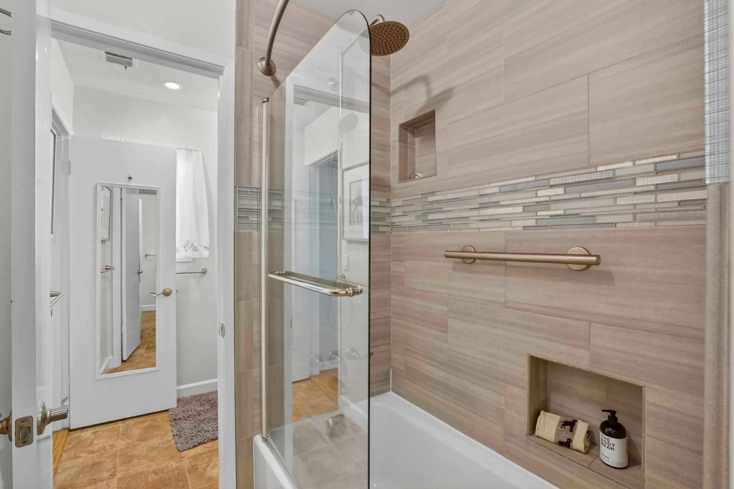Bathroom shower with beige tiles, glass door, built-in shelf, and metal grab bar in 1400 Dolphin Dr., Aptos CA.