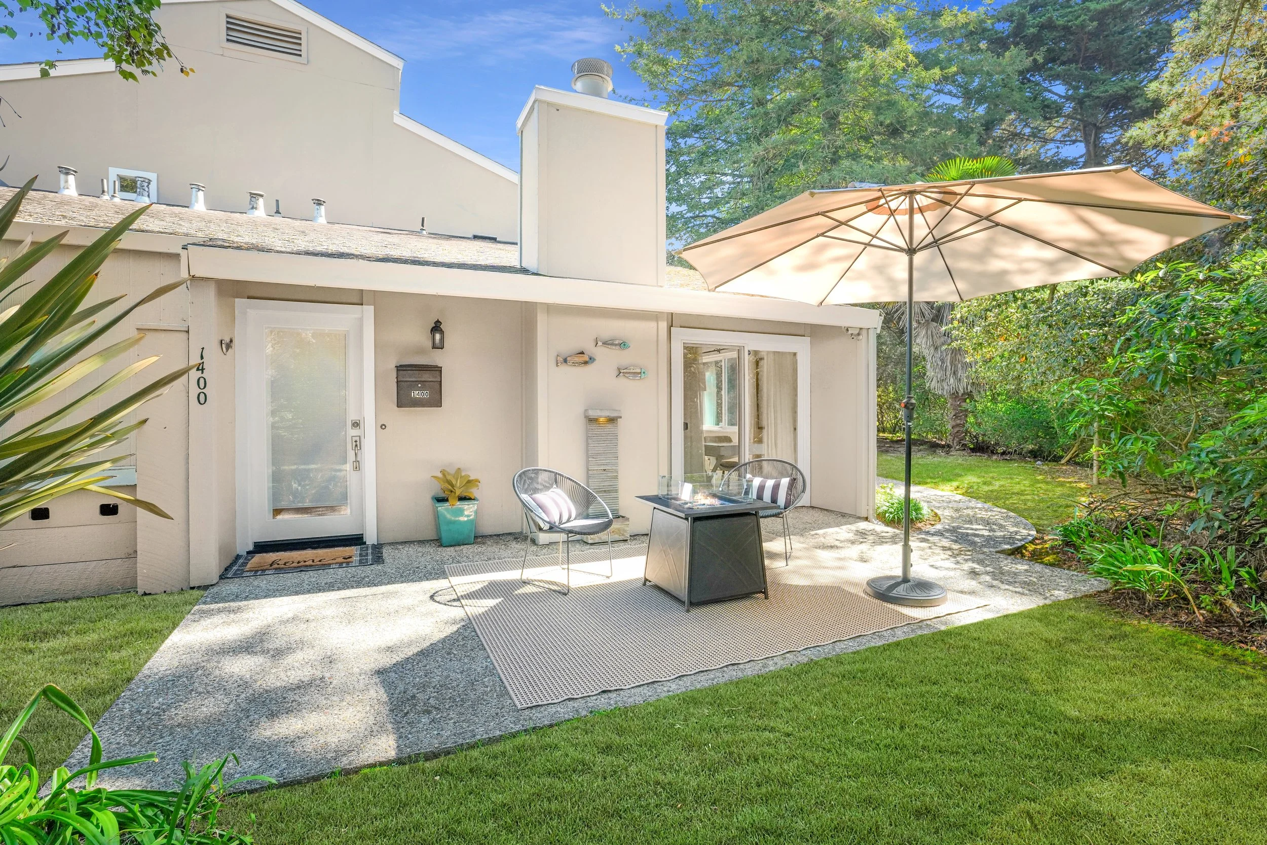 A cozy backyard patio with outdoor seating, an umbrella, and greenery surrounding the area in 1400 Dolphin Dr., Aptos CA.