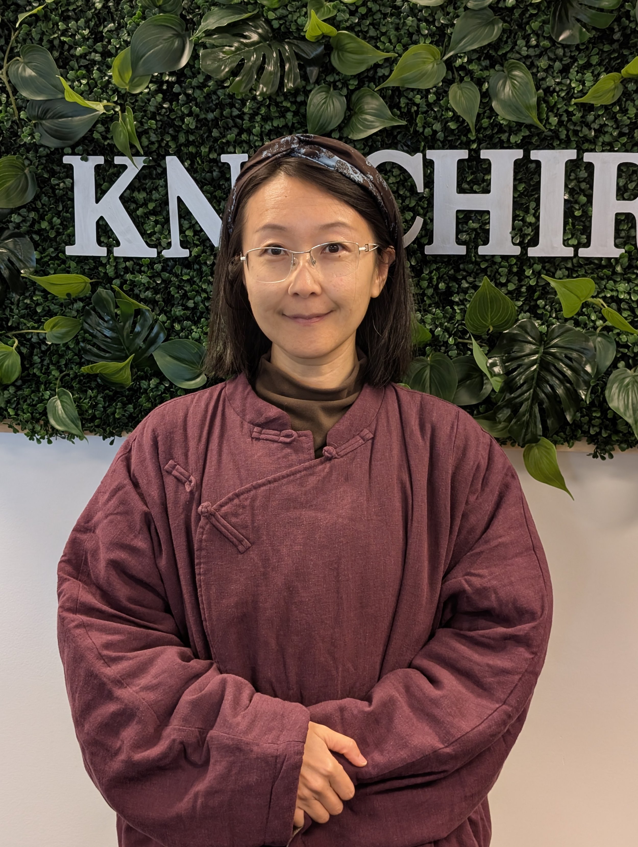 Jing Luo standing in front of green boxwood knfchiro sign with silver letters