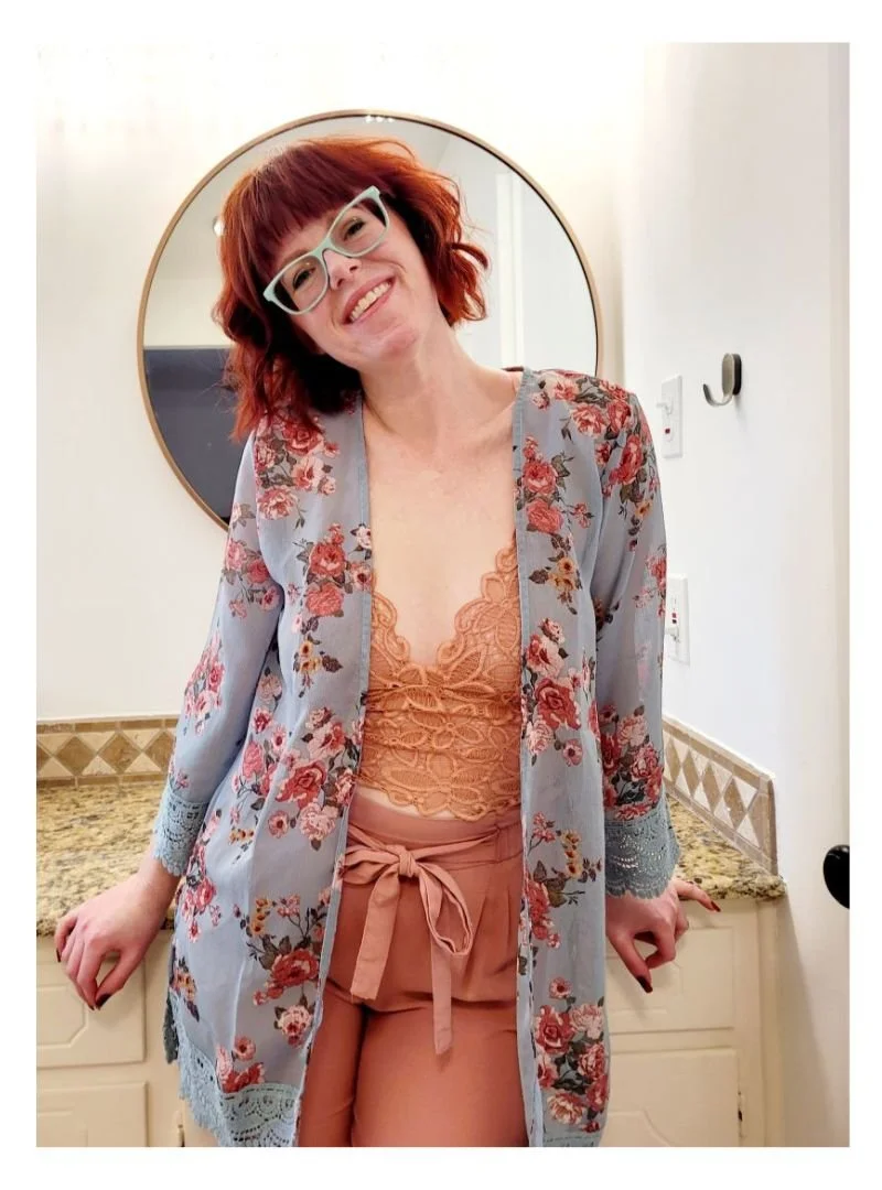 Kate Smith, Website Designer for small businesses wearing a floral lace cardigan over a peach camisole and high-waisted peach pants, standing in a room with a mirror.