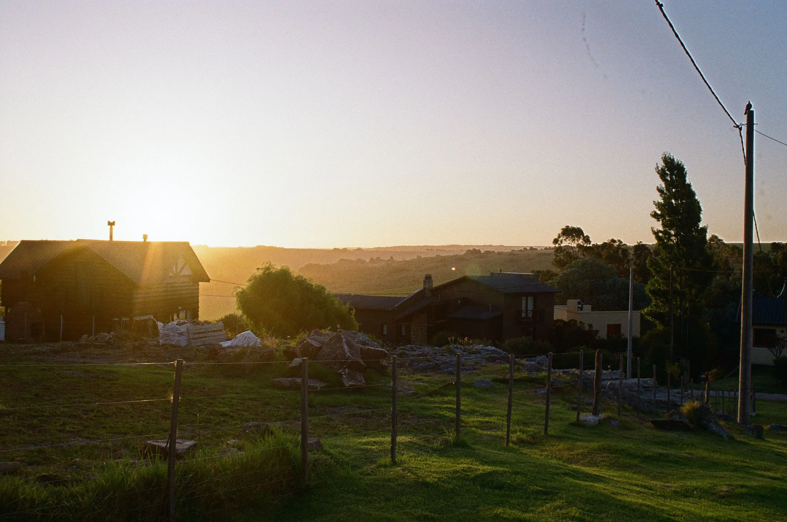 Sunset over a rural residential area with houses, trees, and utility poles.