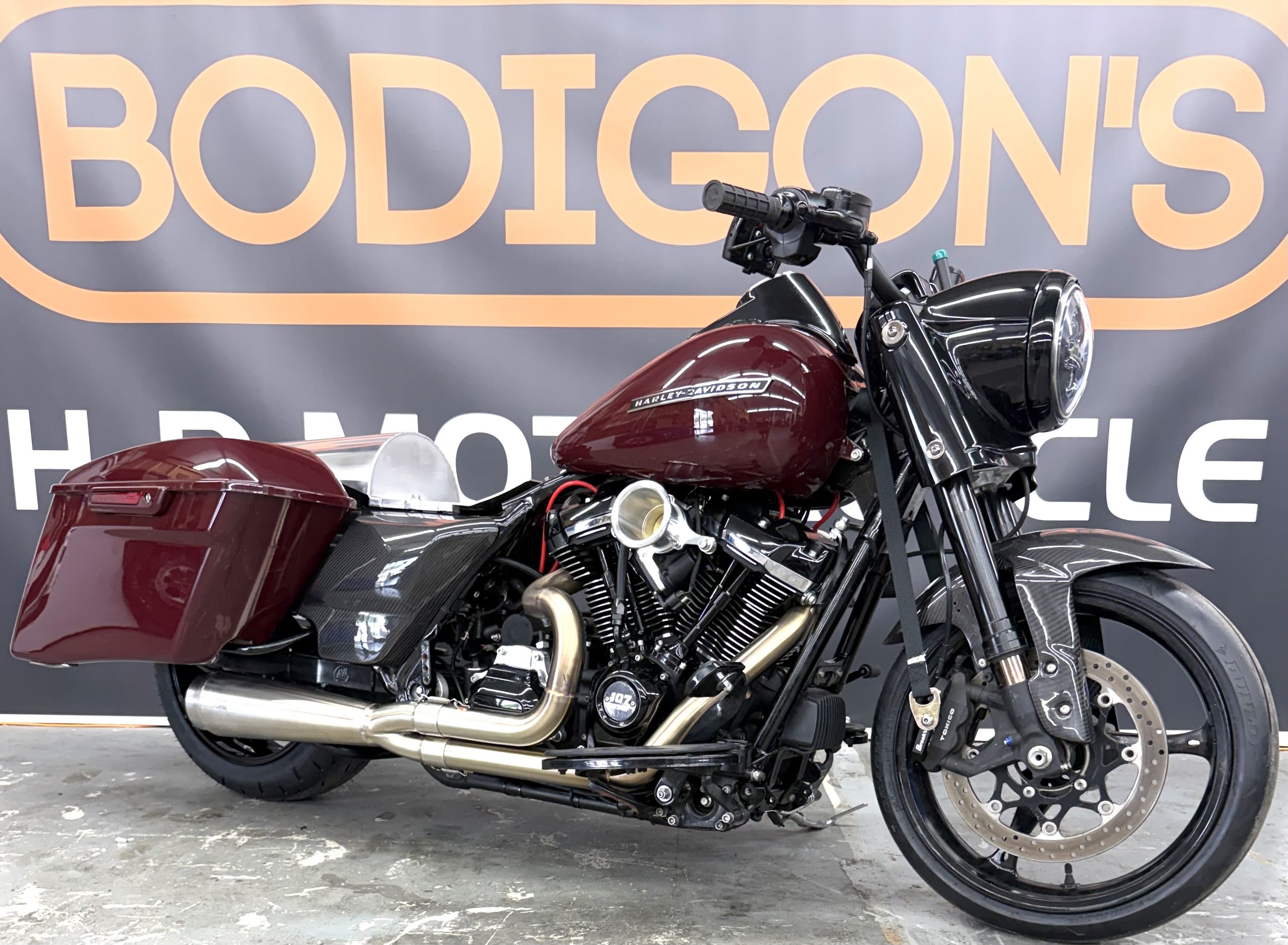 A black and red Harley Davidson motorcycle parked in front of an orange and purple 'BODISONS' sign, with a concrete floor.