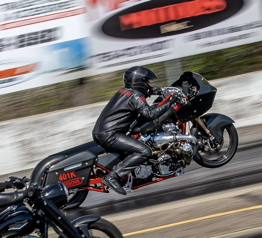 Motorcycle with a rider in black leather suit and helmet speeding down a racetrack.