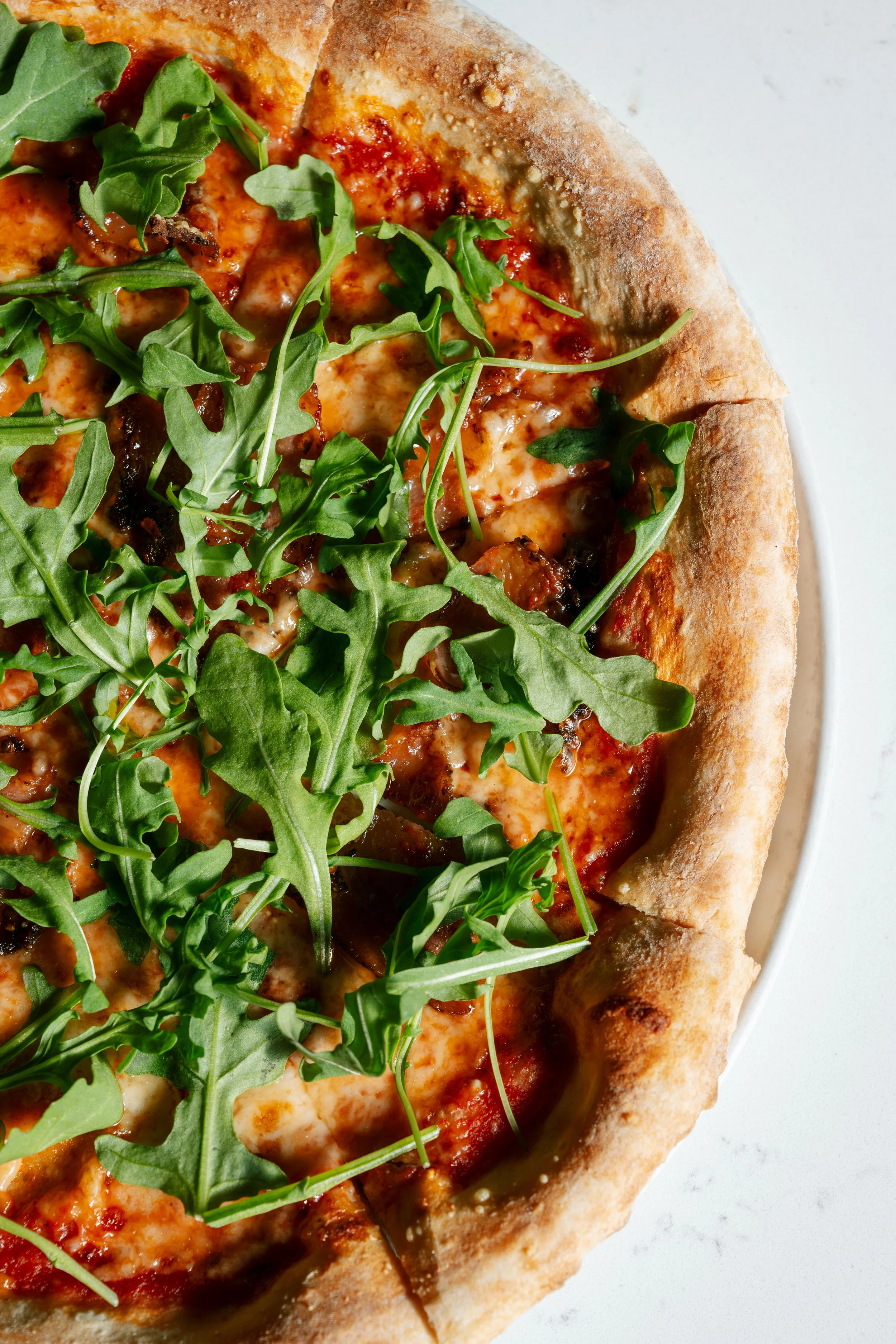 Close-up of a pizza with arugula on top, showing cheese, tomato sauce, and crust edges.