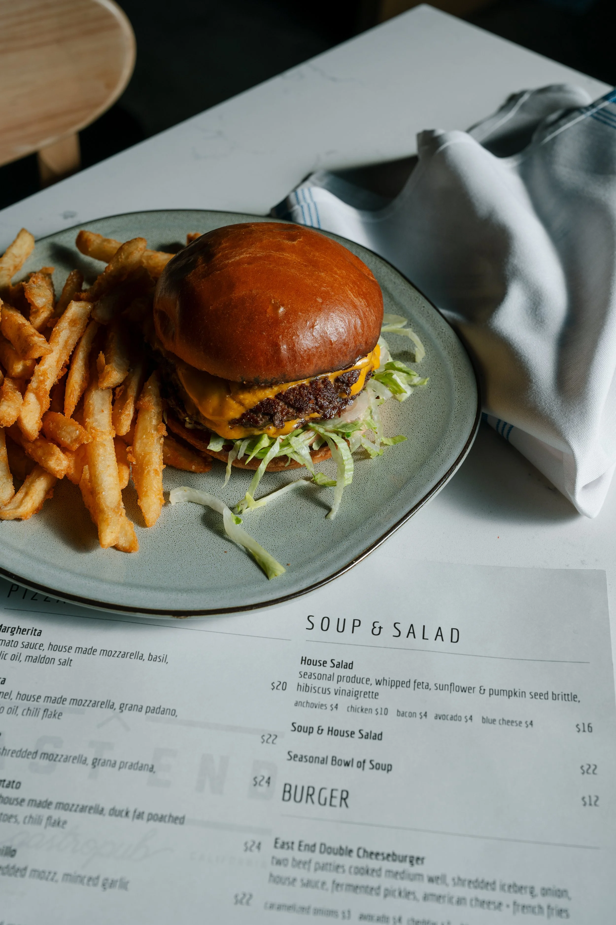 Plate with cheeseburger, French fries, and shredded lettuce, on a table with a napkin and menu underneath.