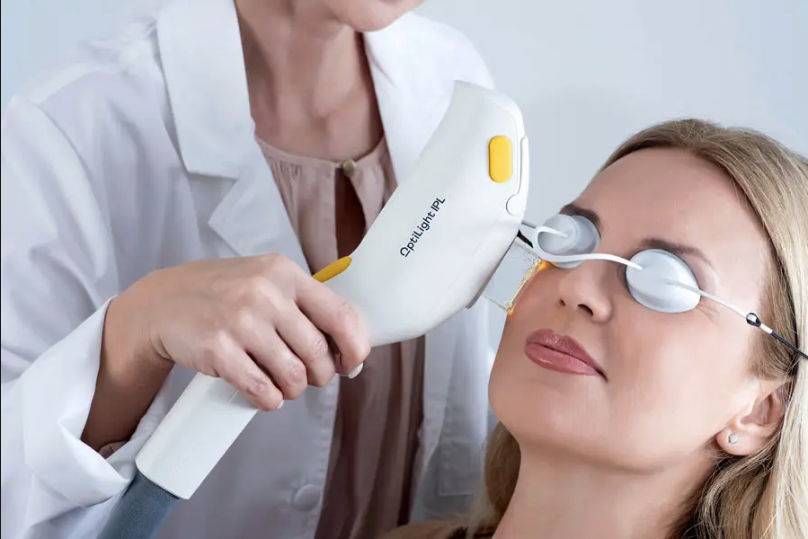 An optometrist uses a specialized IPL device to treat a woman's eyes in a medical office.