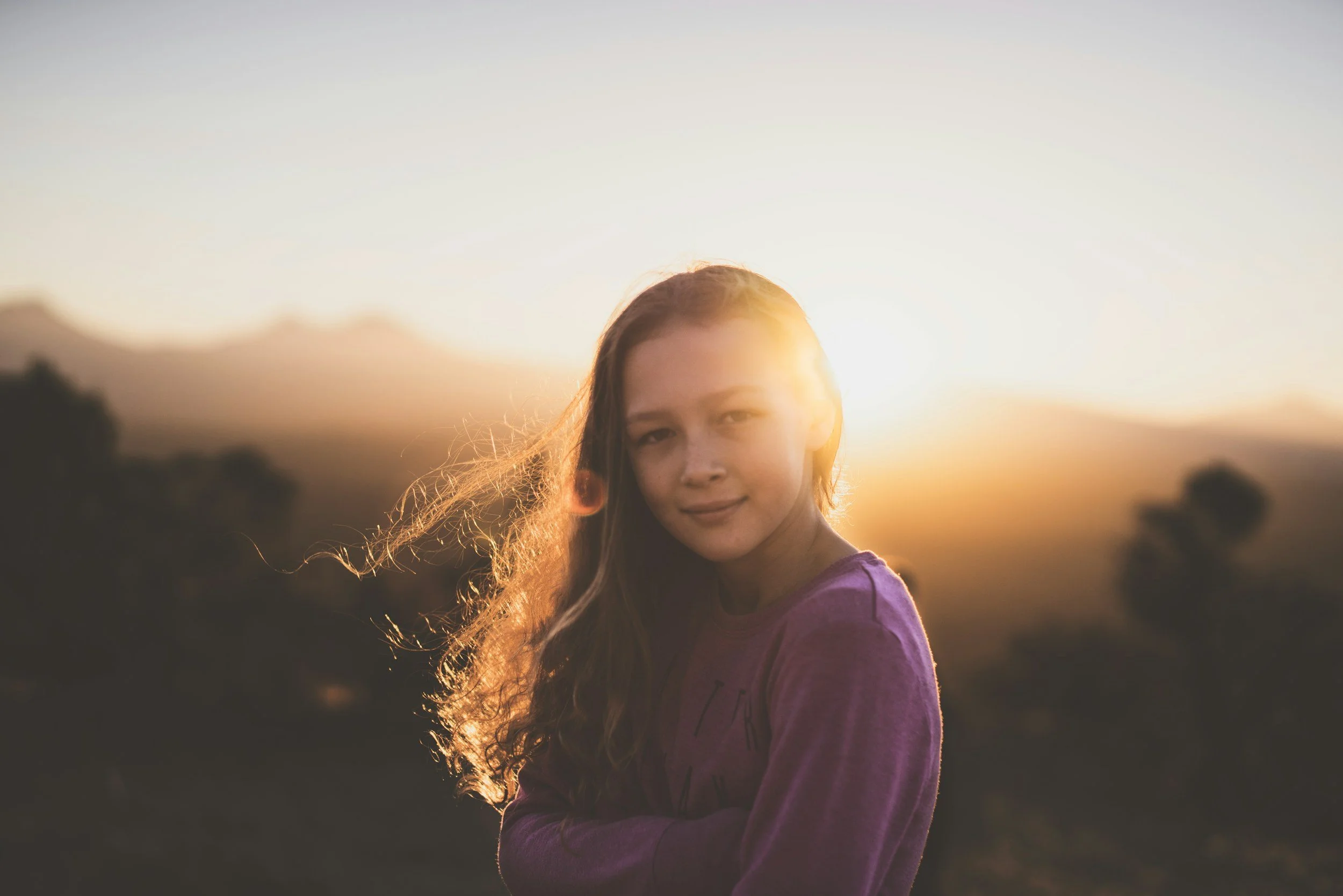 Portrait of a young girl with long hair outdoors during sunset, with a blurred natural background.