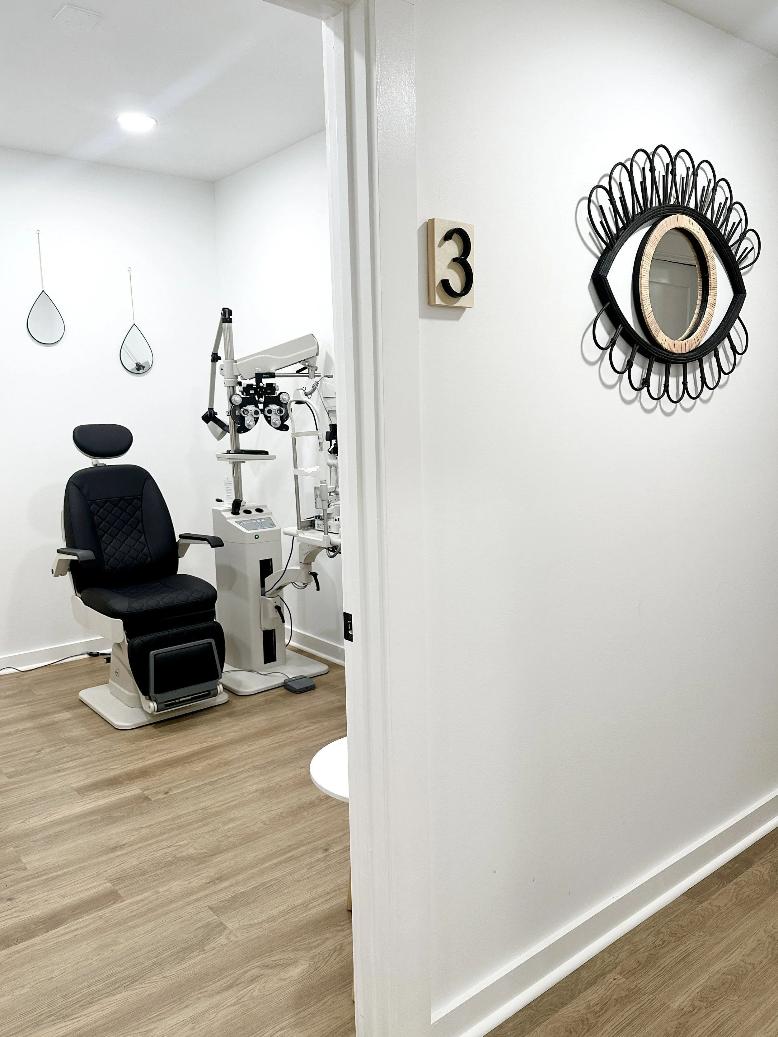 A modern medical examination or treatment room with a black chair, medical equipment, wall decorations, and a wall number 3 sign.