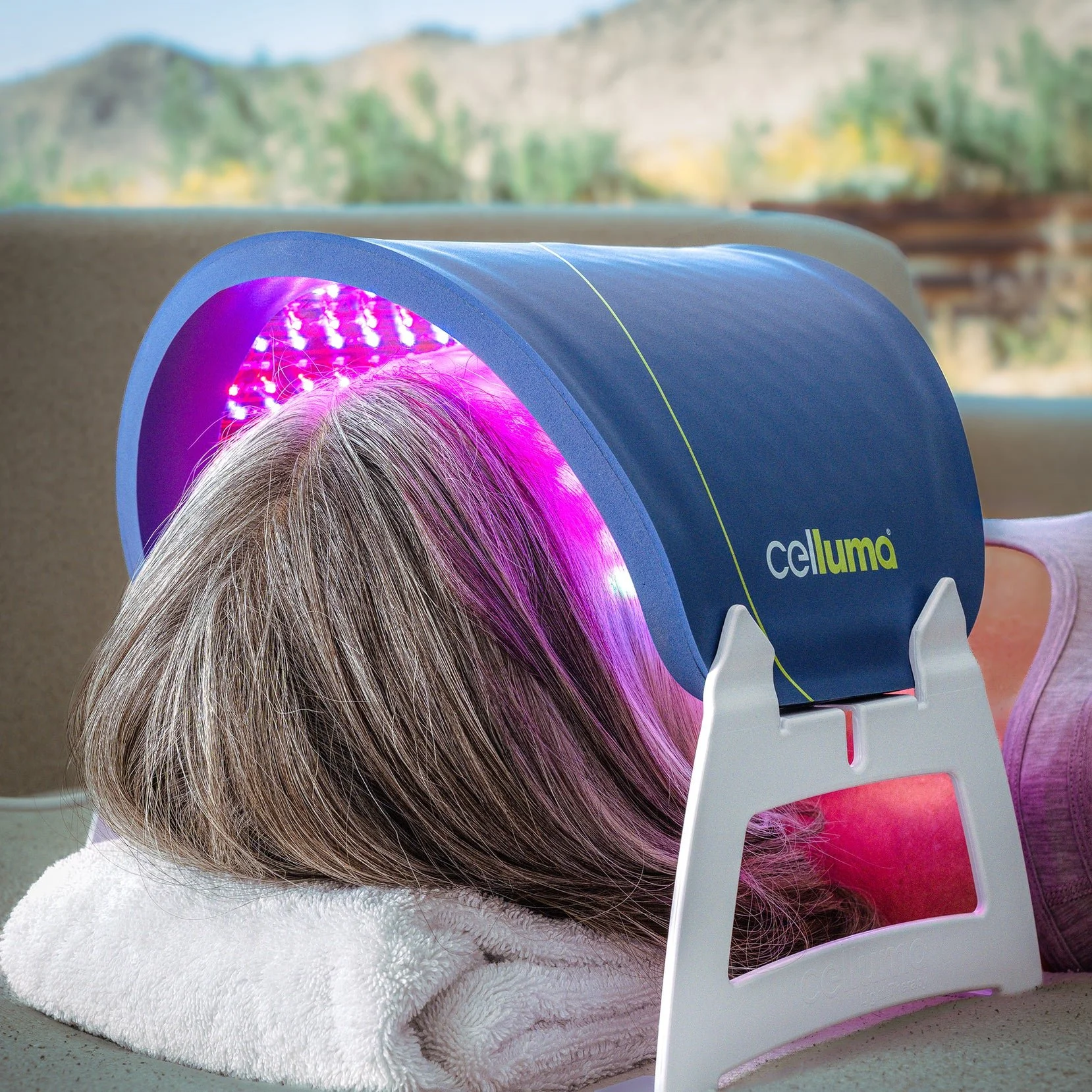 Person with grey hair lying on a towel while undergoing light therapy with a Celluma treatment device emitting purple and pink lights.