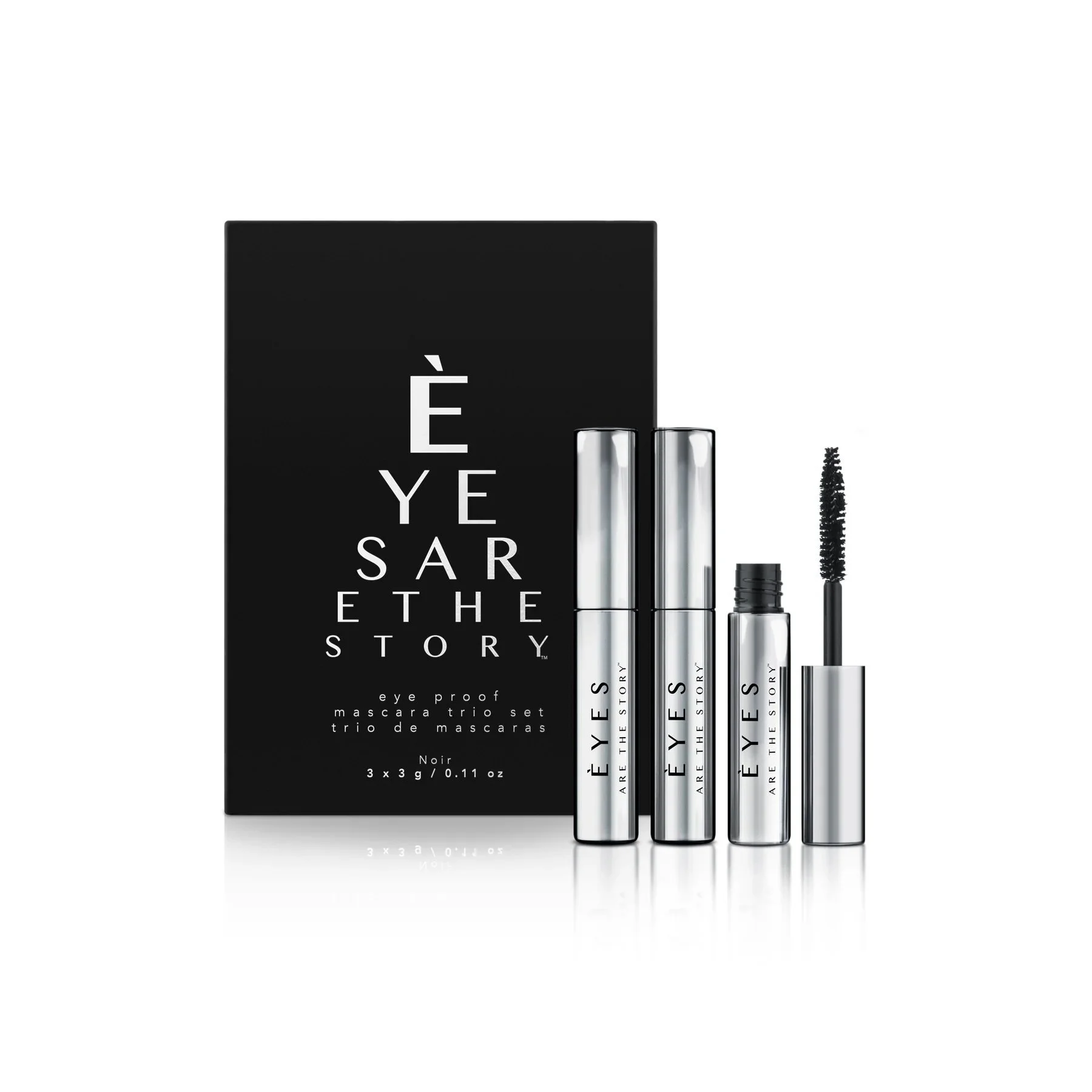Set of three silver and black mascara tubes with a mascara wand, positioned in front of a black box. The box features white text 'ÊYES ARE THE STORY,' and smaller text indicating the mascara is 'eye proof mascara trio set' in French and English.