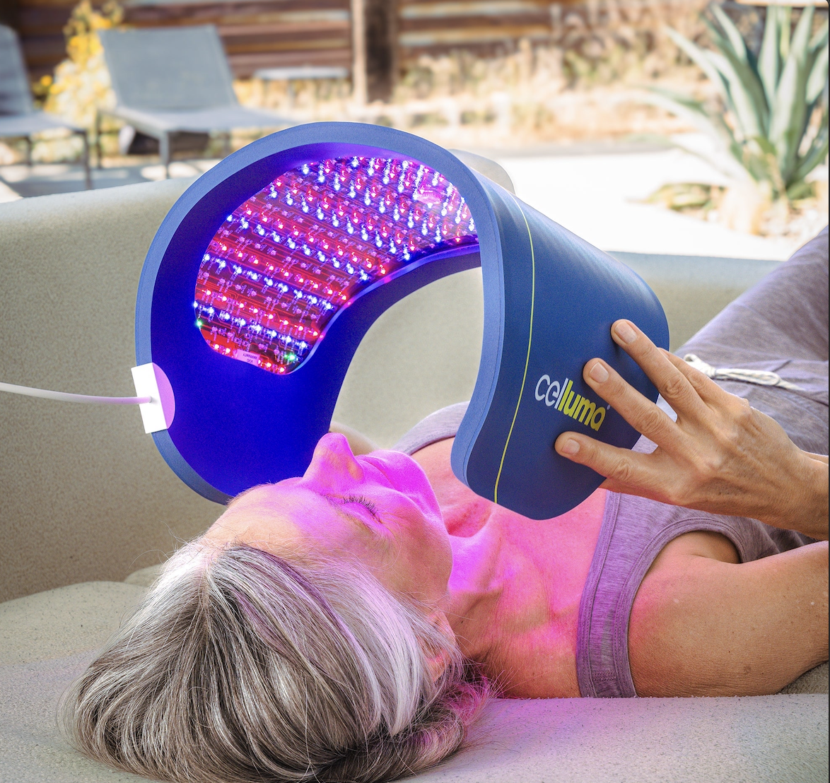 Person receiving red and blue LED light therapy on their face while lying on a beige couch outside.