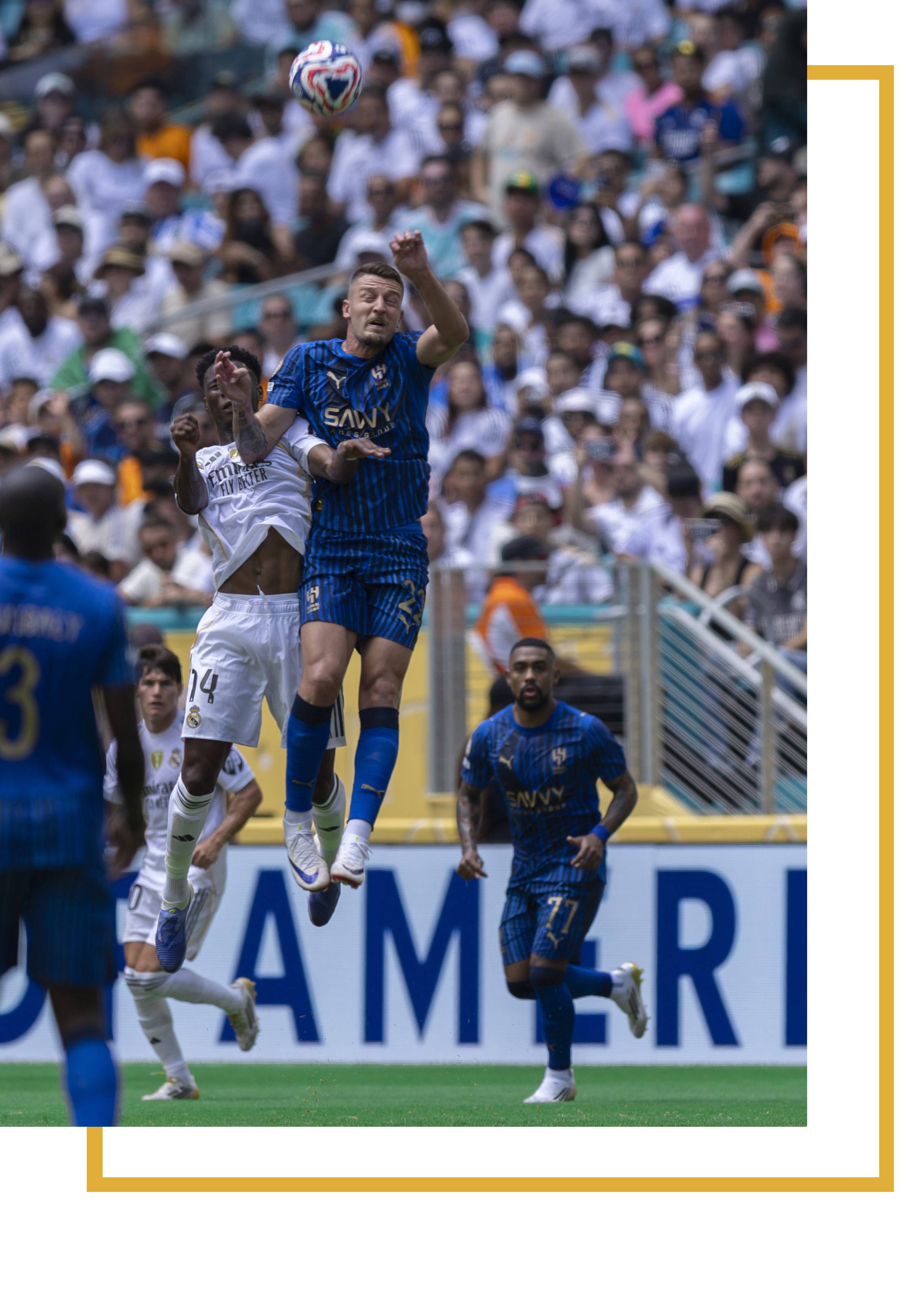 Soccer players competing for the ball during a match, with crowd in the background.