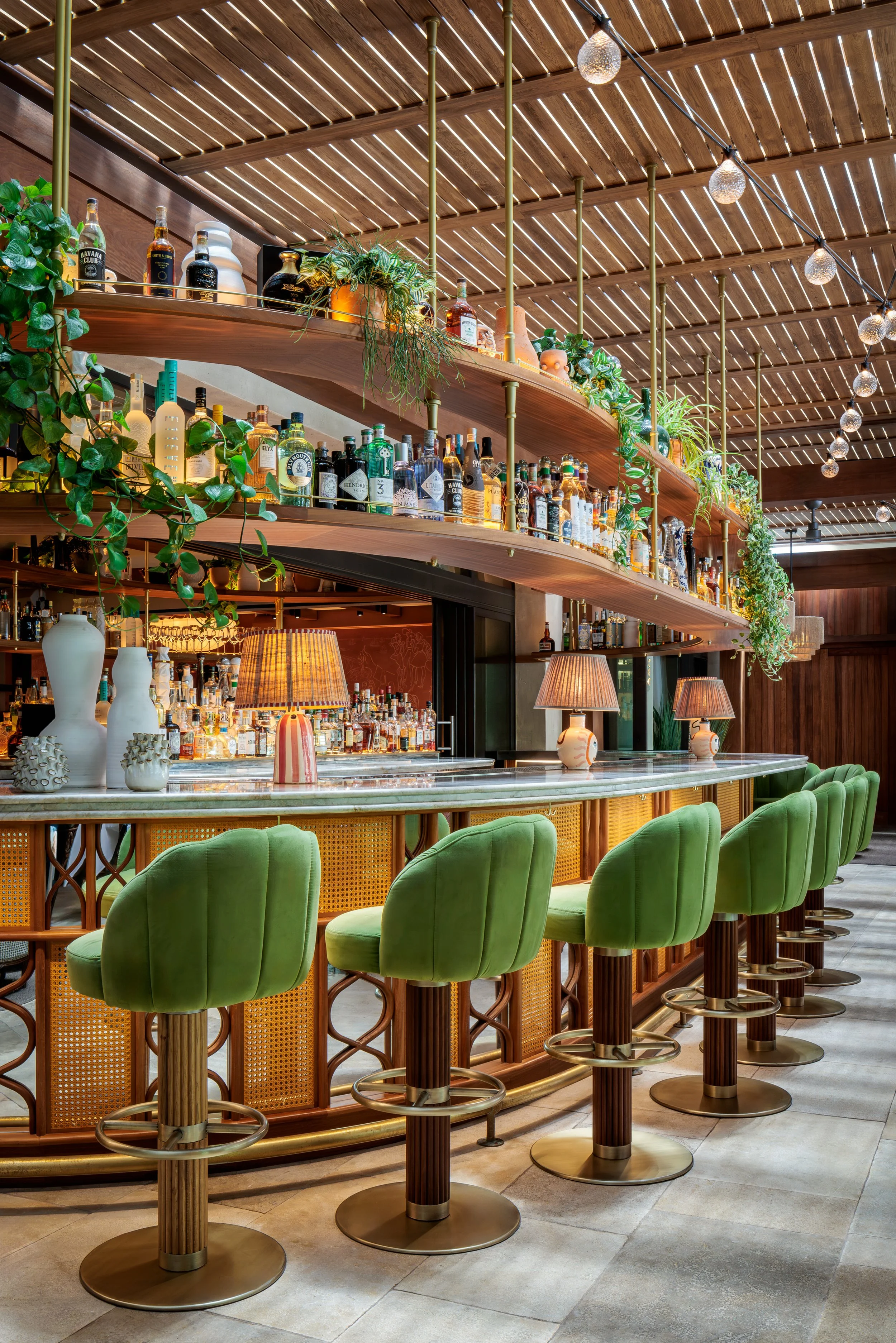 CLAUDIE's elegant bar with green barstools, plants hanging and a full stacked bar.