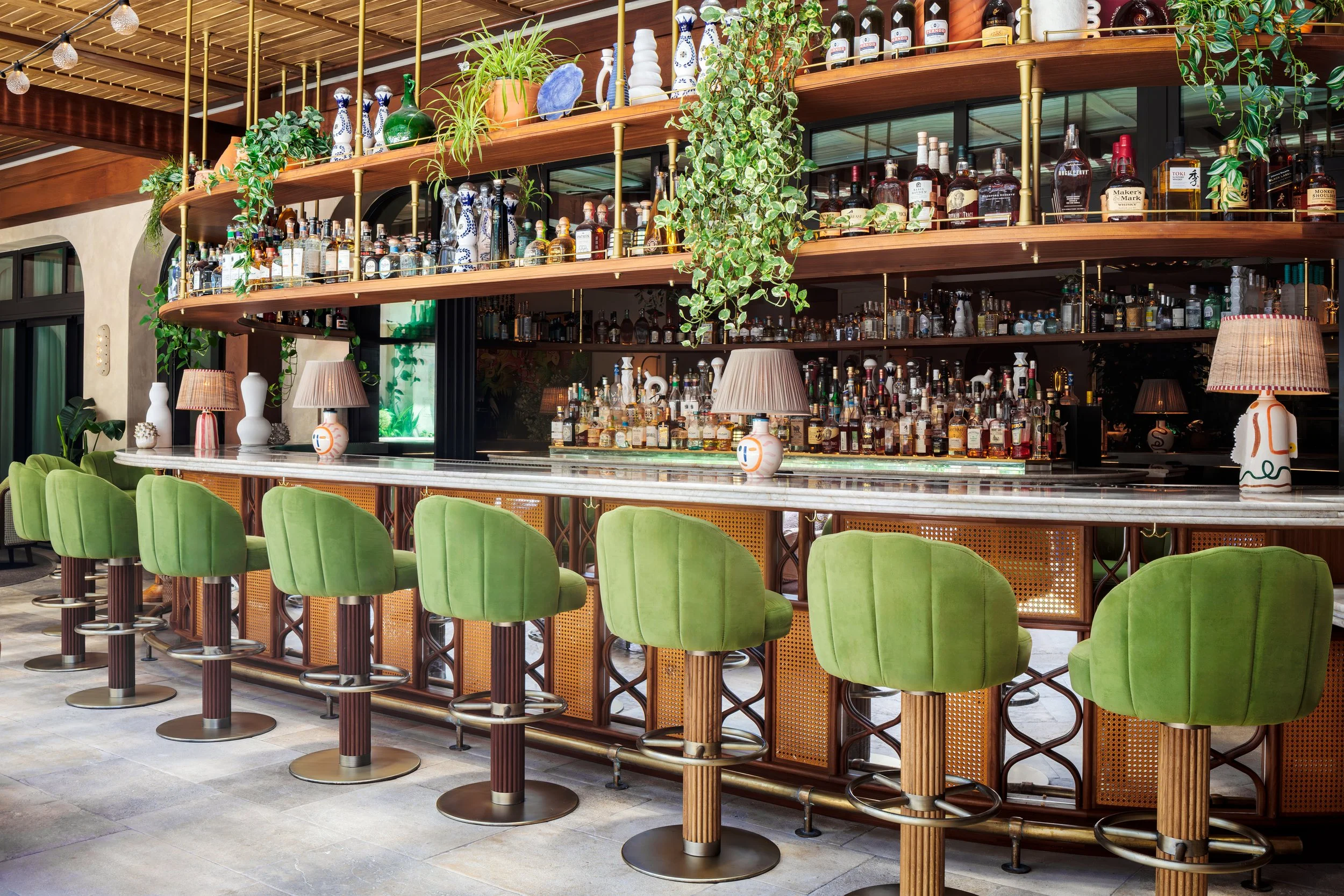 CLAUDIE's outdoor bar with green barstools, a fully stacked bar, and green plants near the alcohol.