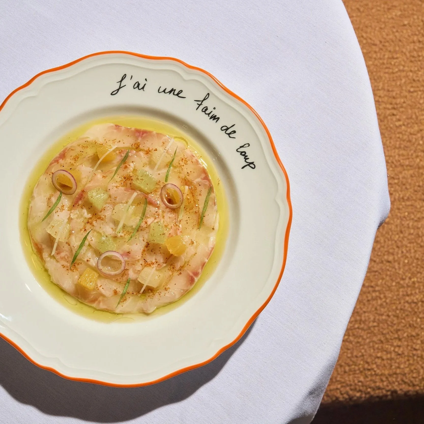 Entree dish of branzino carpaccio garnished with vegetables on a table at Claudie restaurant,