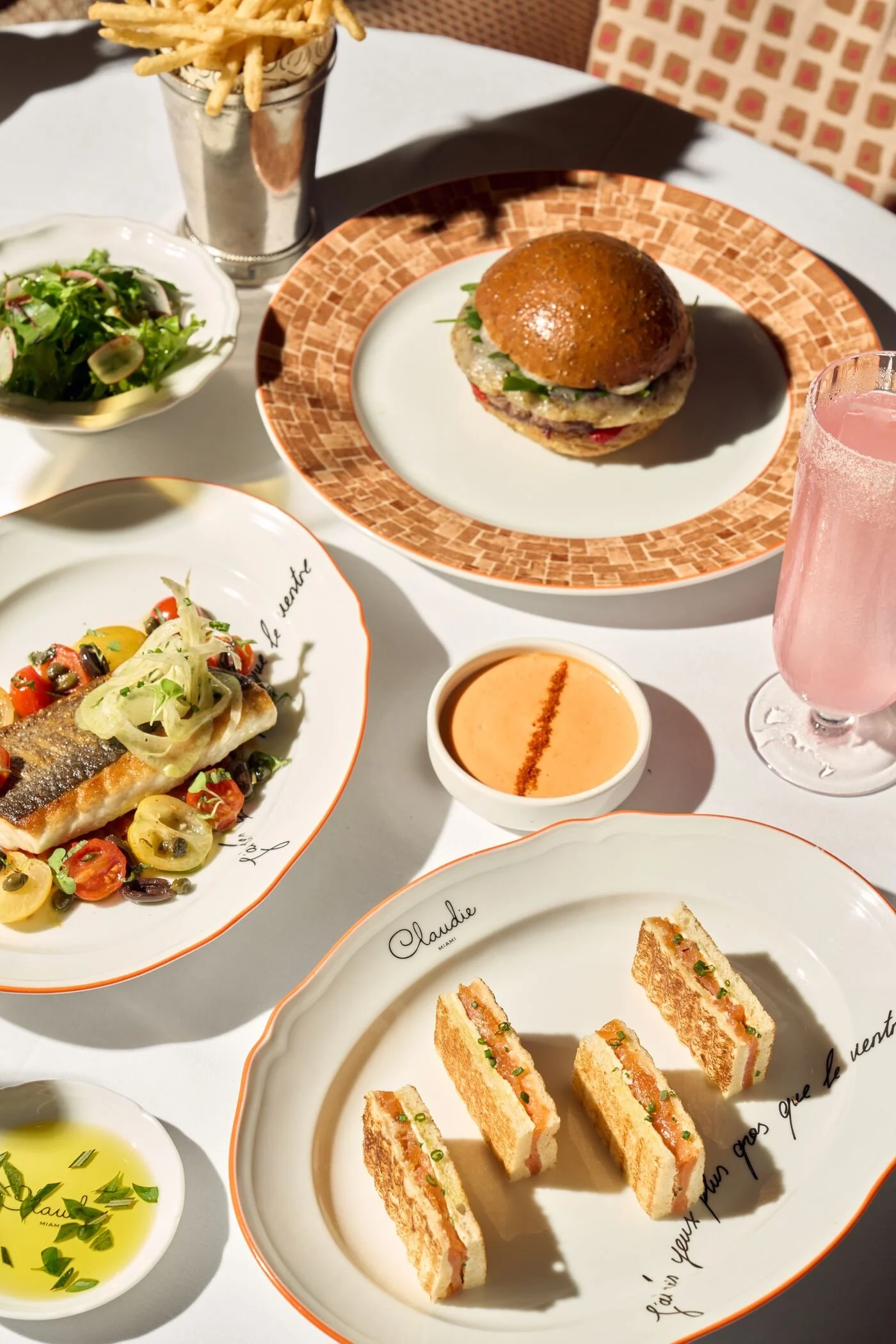 CLAUDIE's menu items for lunch, including a fish, sandwiches, and a pink cocktail.