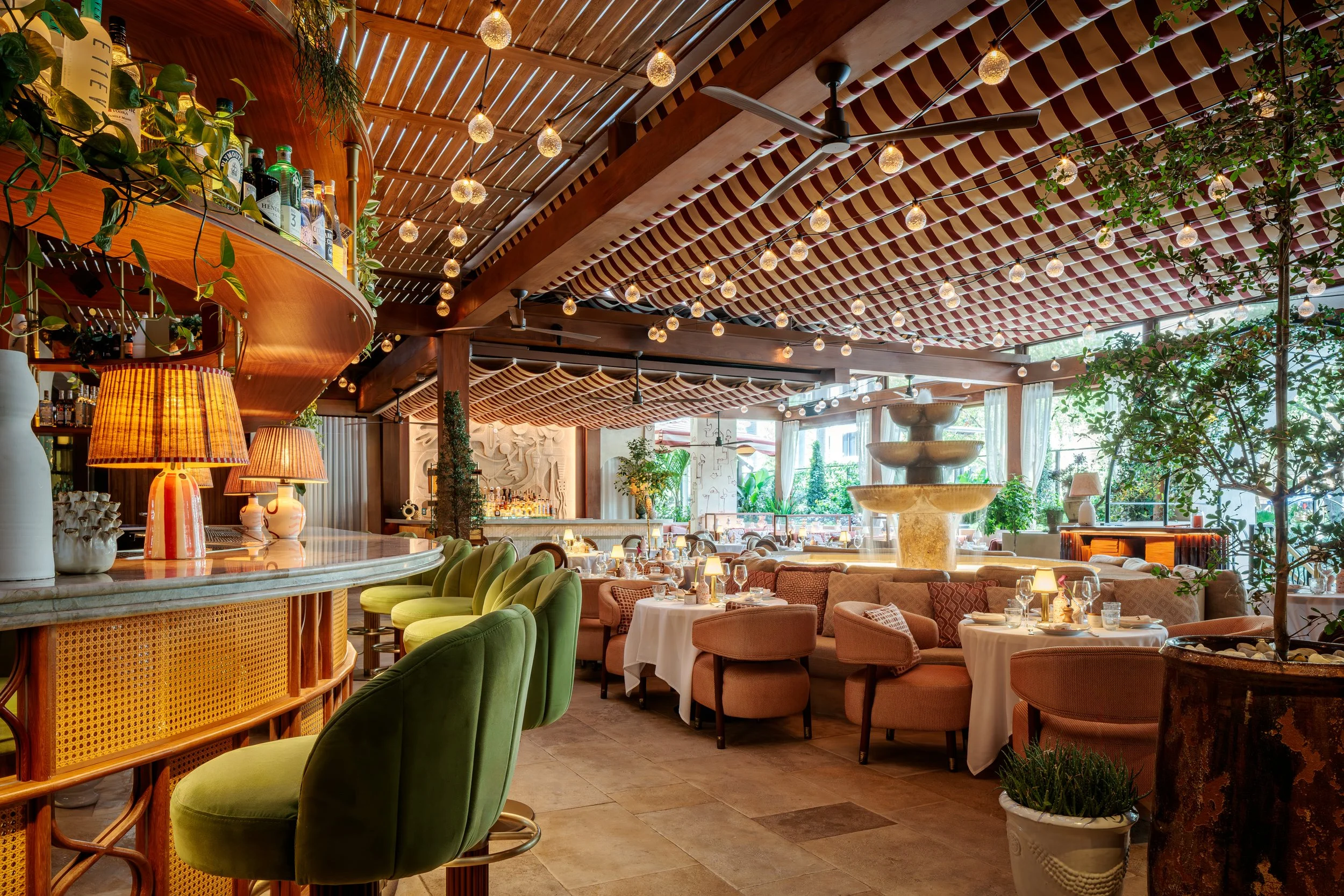 Interior dining setting of Claudie restaurant with vibrant interior decorations including plants, a fountain and lights.