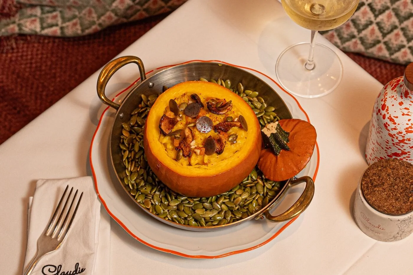 Gourmet pumpkin dish topped with seeds and crispy garnishes, served in a pan at a restaurant table