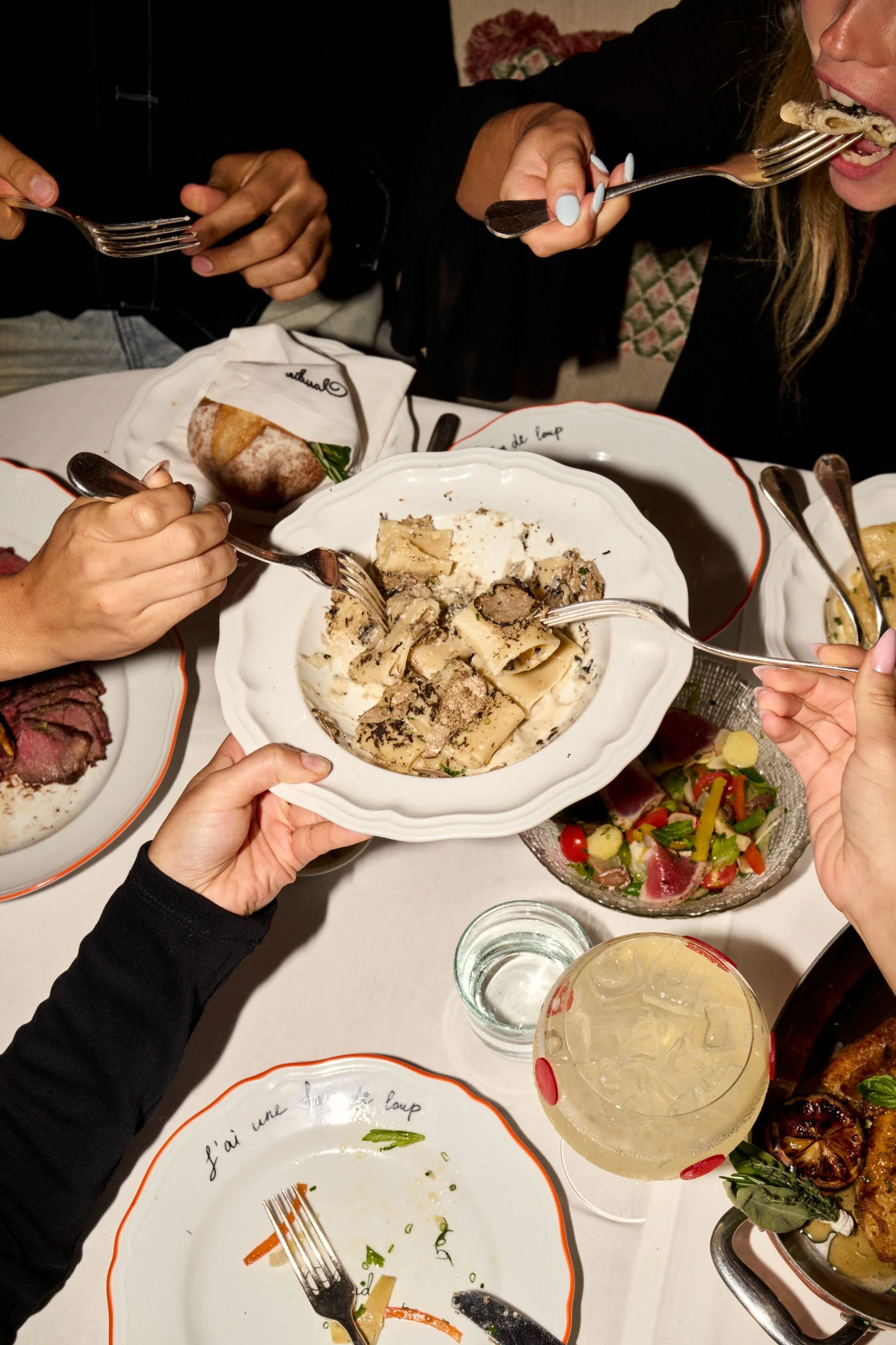 Four people dining at one of CLAUDIE"s tables, sharing a pasta dish.