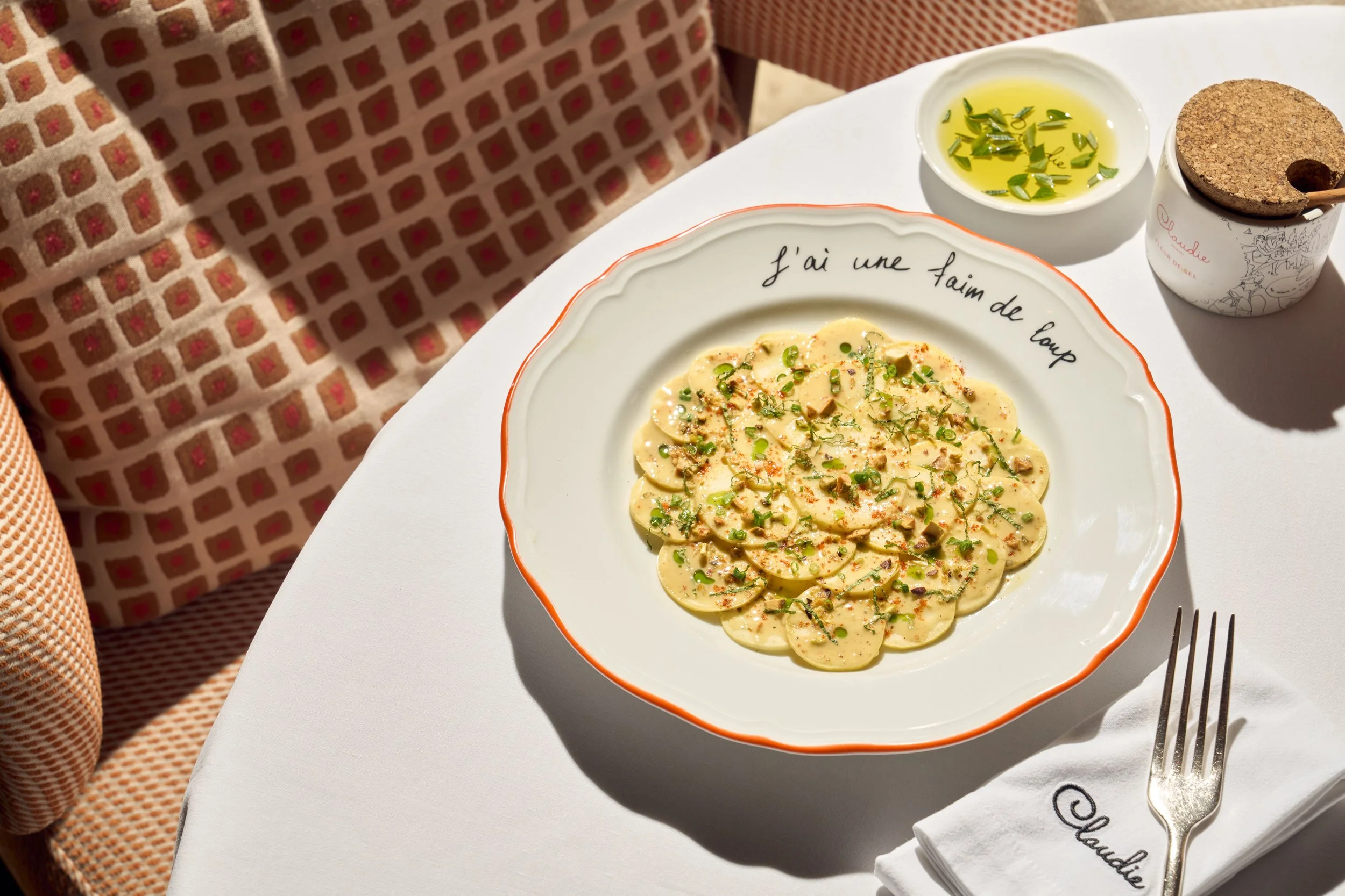 Menu item at CLAUDIE that is on a table, with a pasta dish garnished with greenery with a side of olive oil and salt.