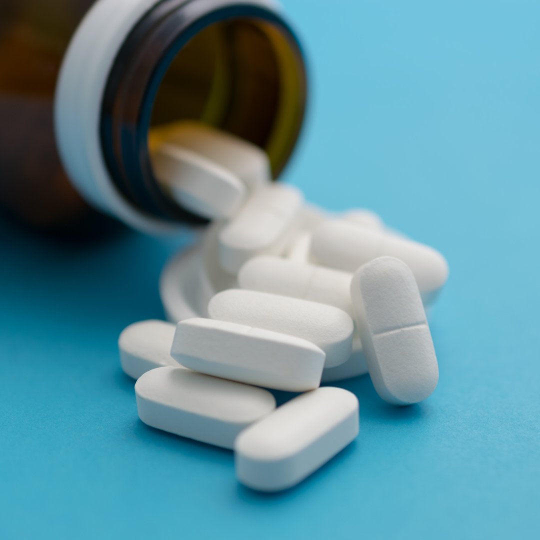 White oblong pills spilled out of an open amber pill bottle onto a blue background, representing psychiatric medication management | Blue Lotus Telepsychiatry Services, Inc.