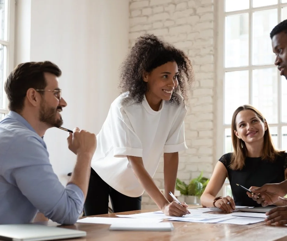 Four smiling professionals collaborate around a conference table reviewing documents together | Blue Lotus Telepsychiatry Services, Inc.