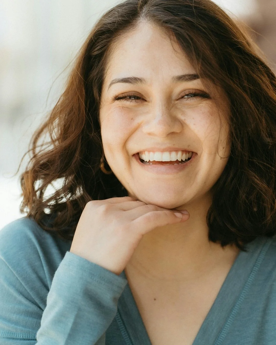 A woman laughs warmly with her chin resting on her hand in a close-up portrait | Blue Lotus Telepsychiatry Services, Inc.