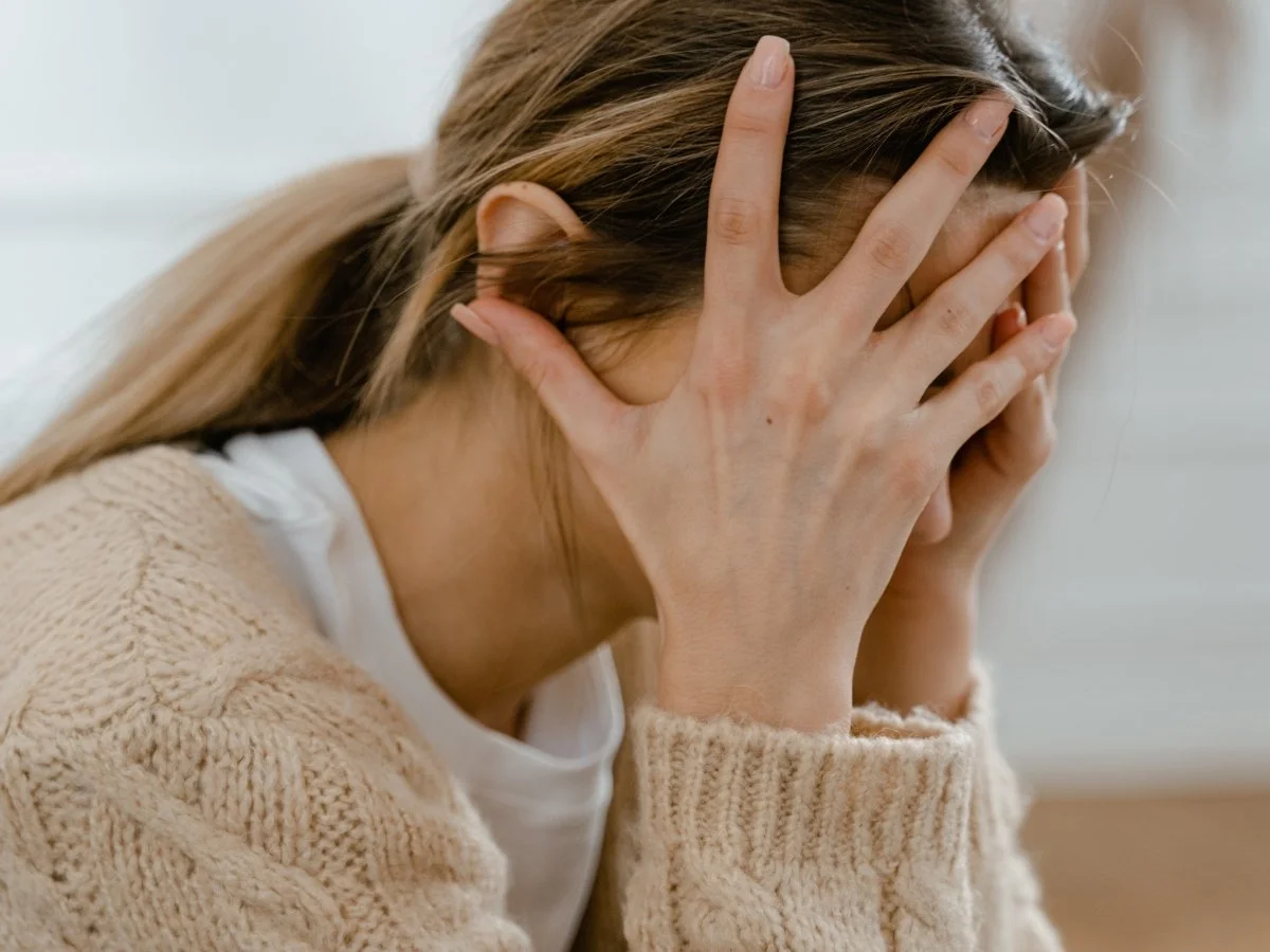 A woman covers part of her face with her hand as her hair falls forward, hiding her expression | Blue Lotus Telepsychiatry