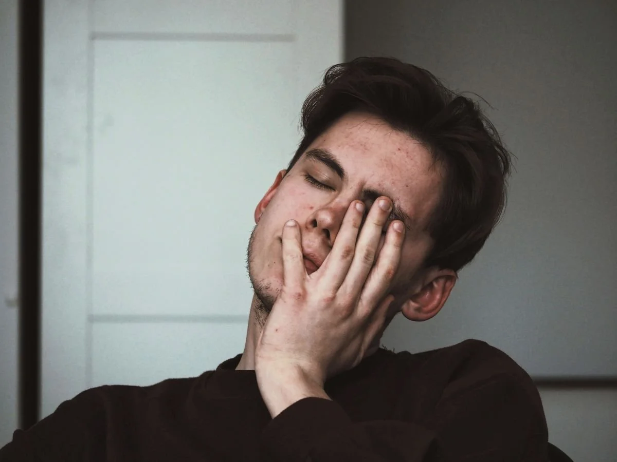 A young man closes his eyes and rests his hand against his face with a pained expression | Blue Lotus Telepsychiatry