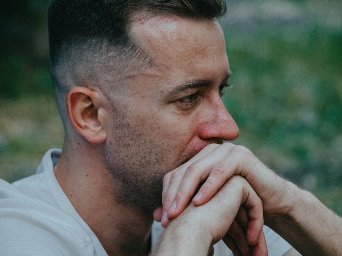 A man in profile rests his clasped hands near his chin, gazing off with a pensive expression | Blue Lotus Telepsychiatry