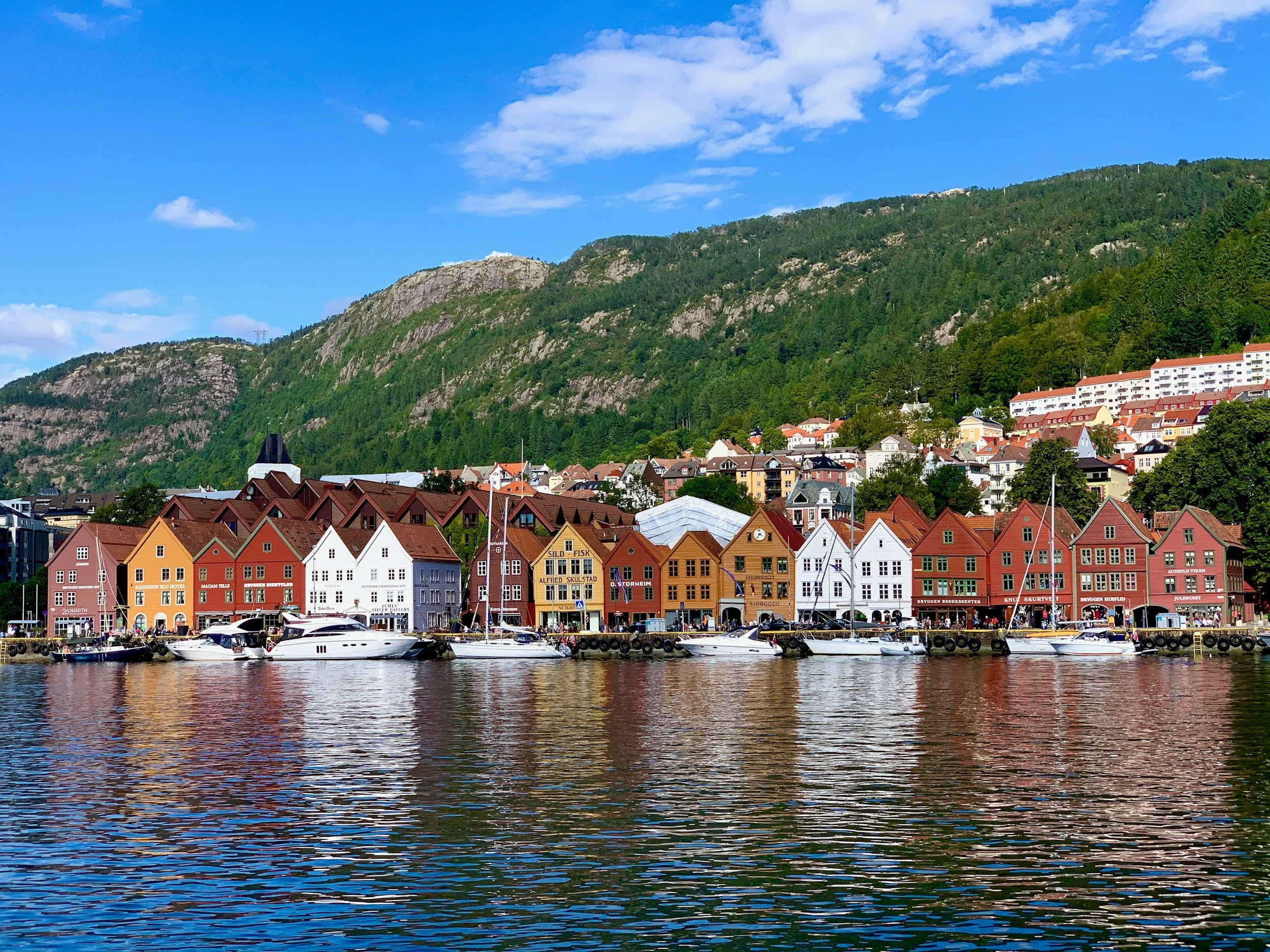 Aerial view of a coastal area in Norway showing islands, a bridge connecting landmasses, and a small town with white buildings.
