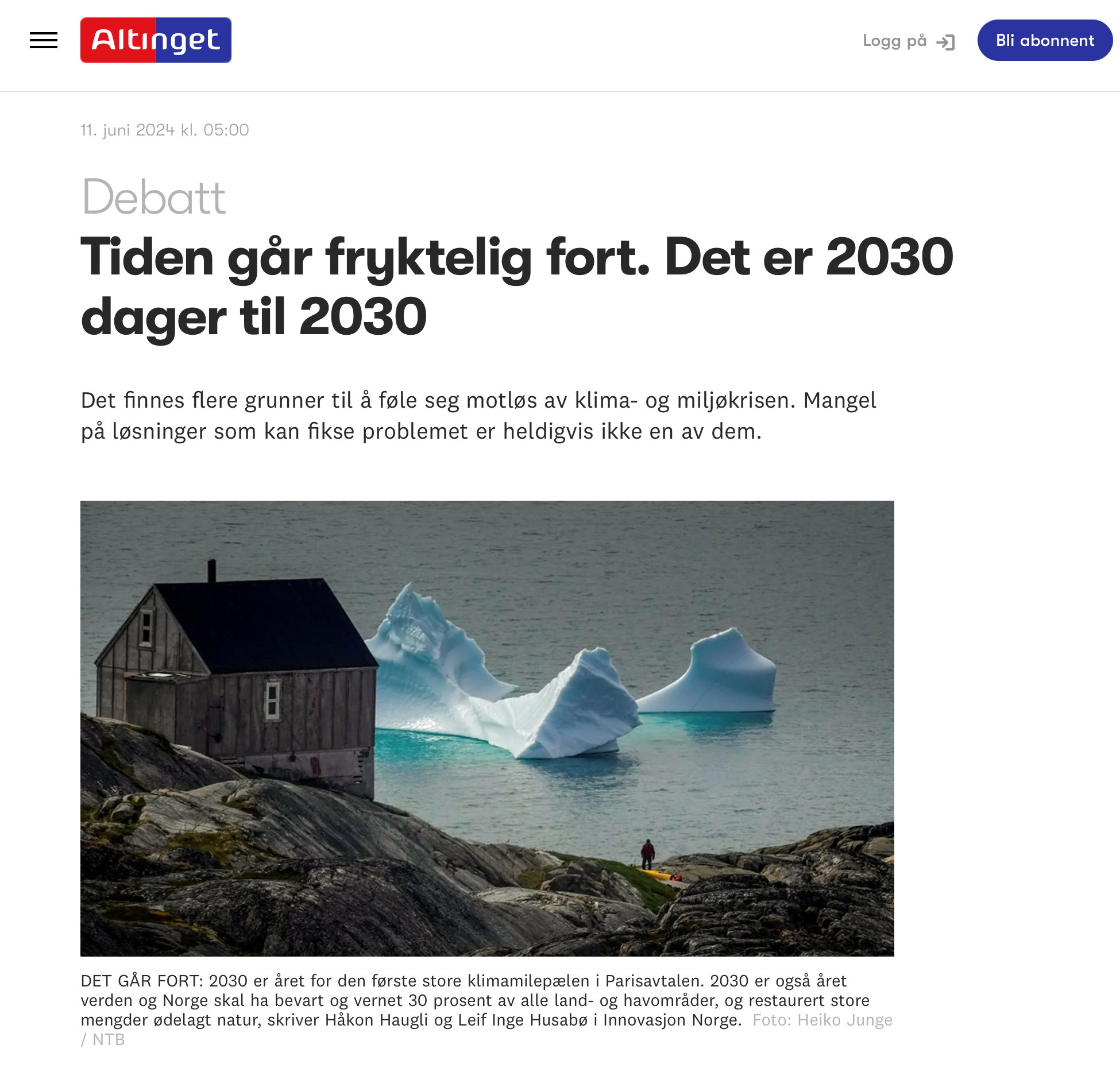 Iceberg floating near a wooden cabin on rocky coast with a person standing nearby.