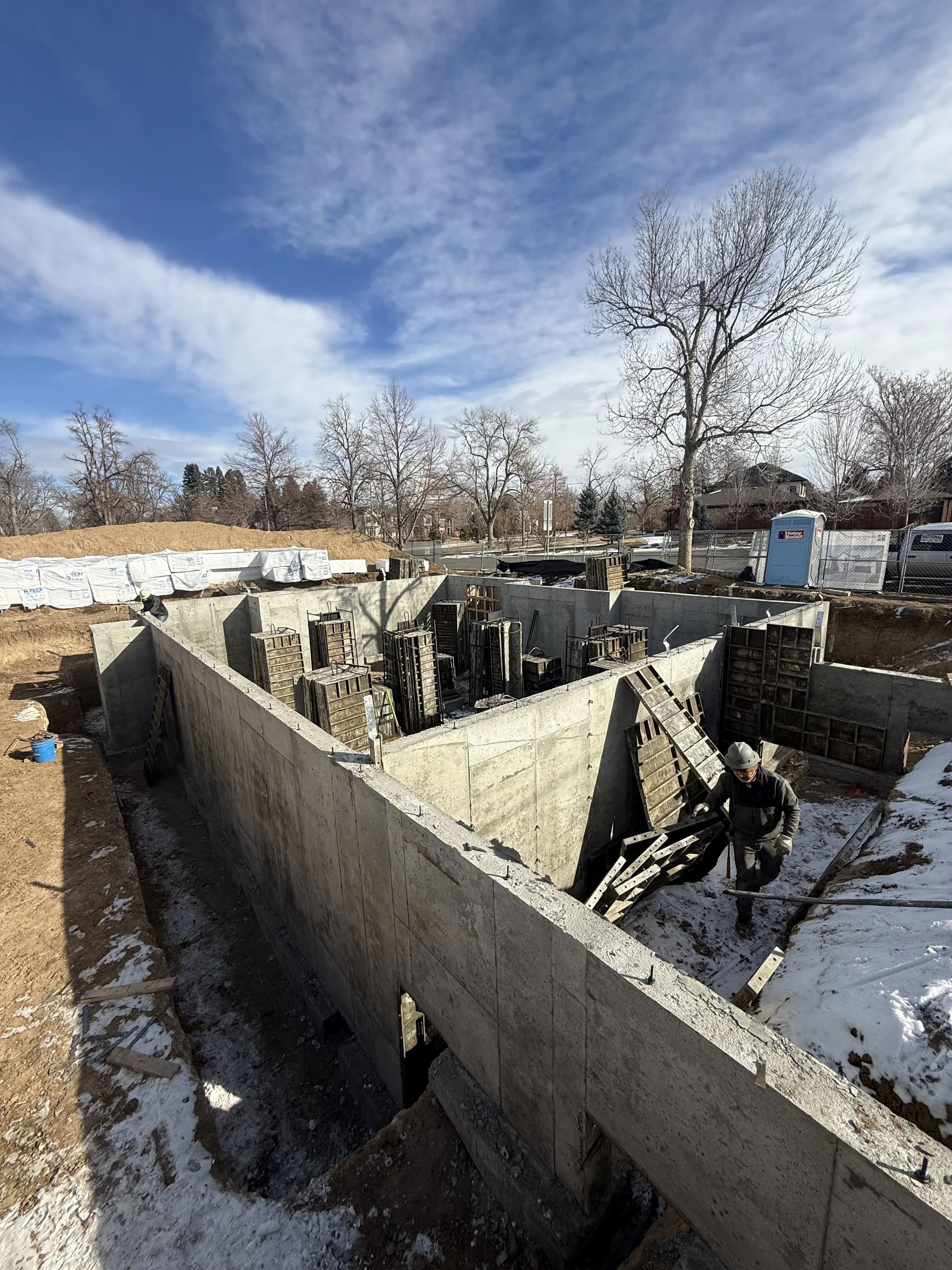 The Elizabeth Victorian-style home addition. Mid-construction with concrete walls and a worker surrounded by wooden forms and construction equipment.