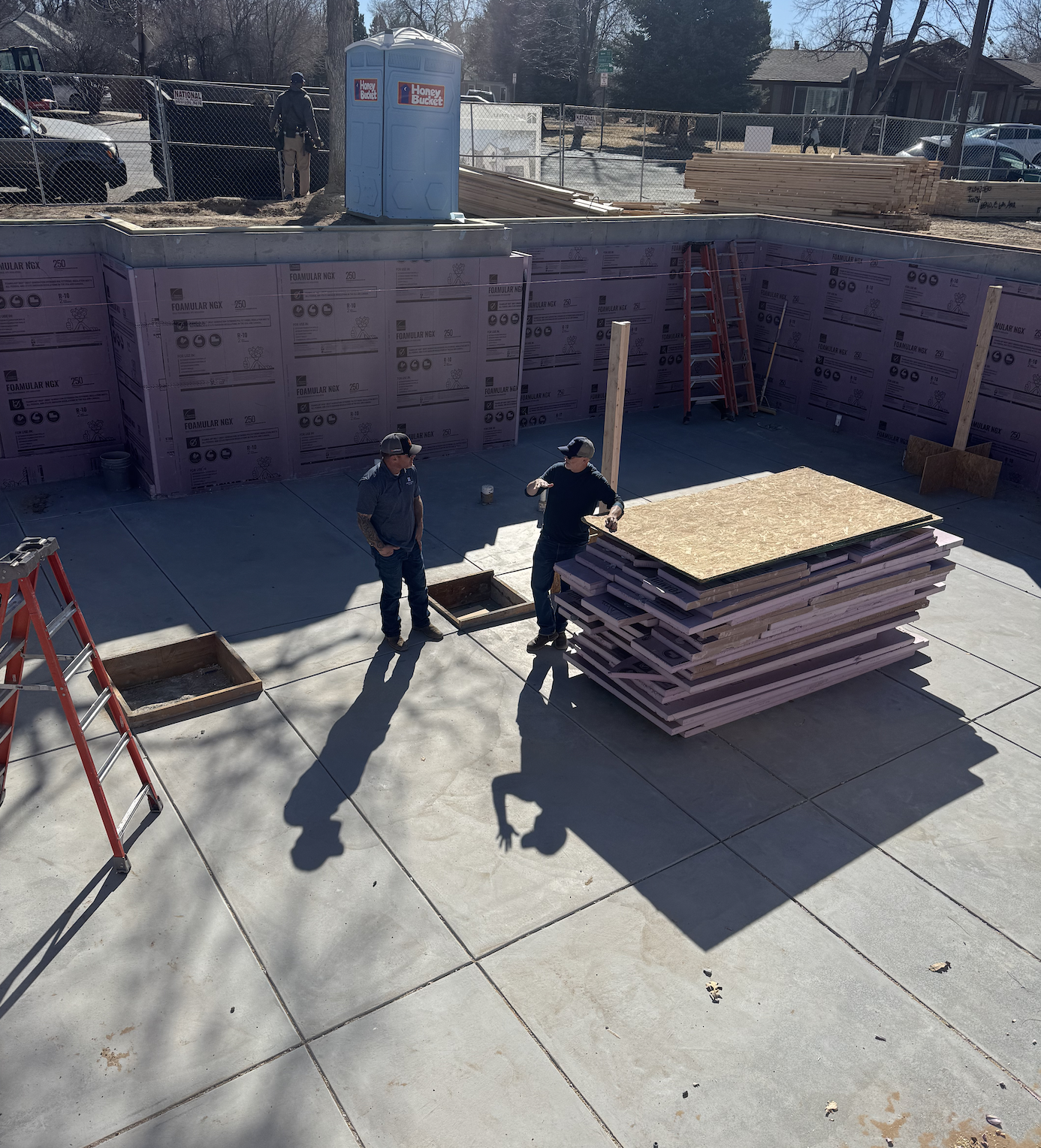The Elizabeth Victorian-style home addition. Mid-project construction workers with stacked plywood and framing materials, surrounded by construction equipment