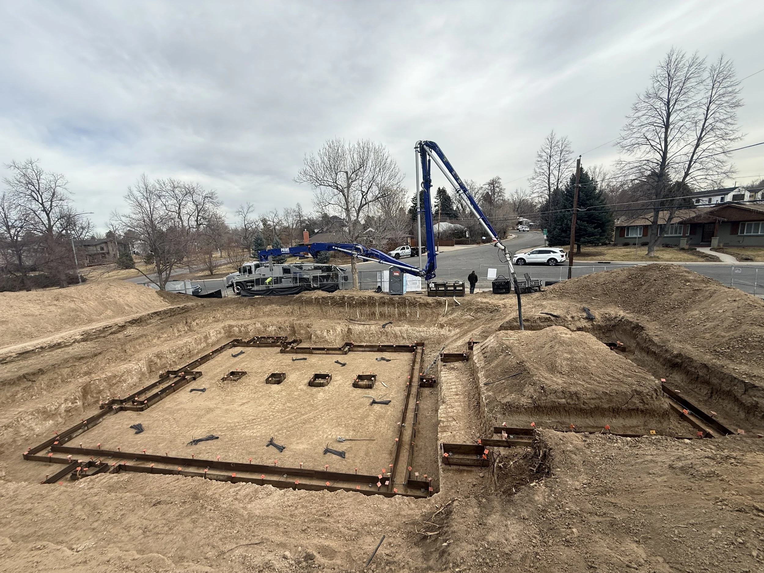 The Elizabeth Victorian-style home addition. Mid-project construction site with foundation and steel reinforcements being prepared and a concrete pump truck pouring concrete. 