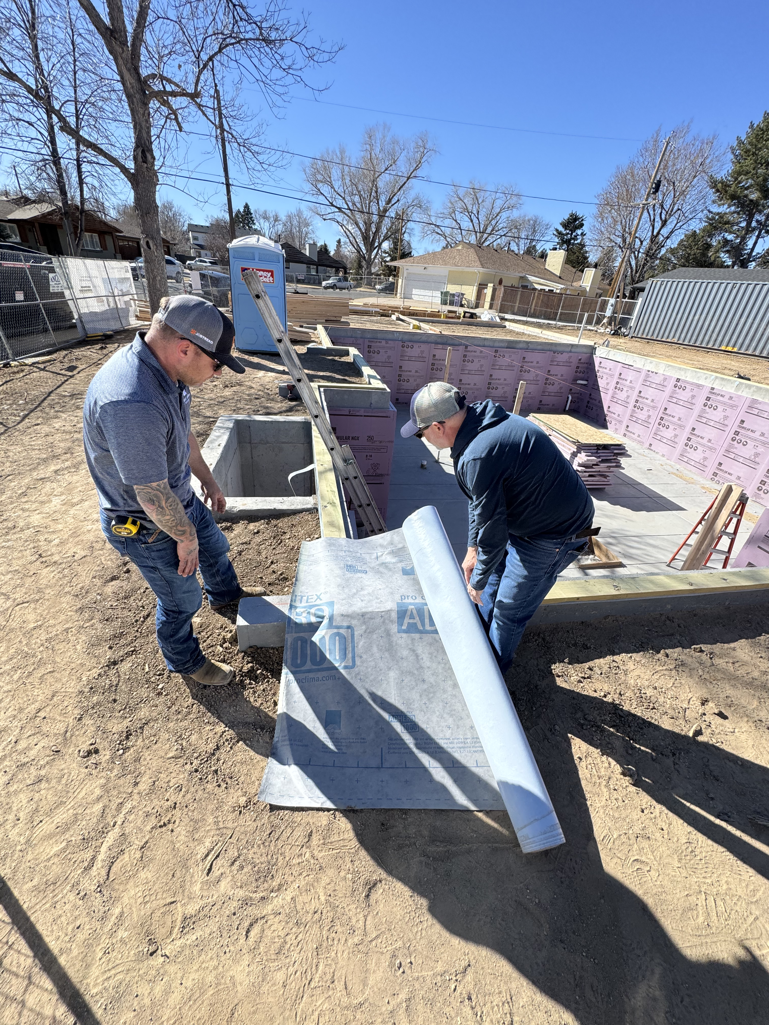 The Elizabeth Victorian-style home addition. Mid-project construction workers are working on foundation walls at a building site under a clear blue sky. 