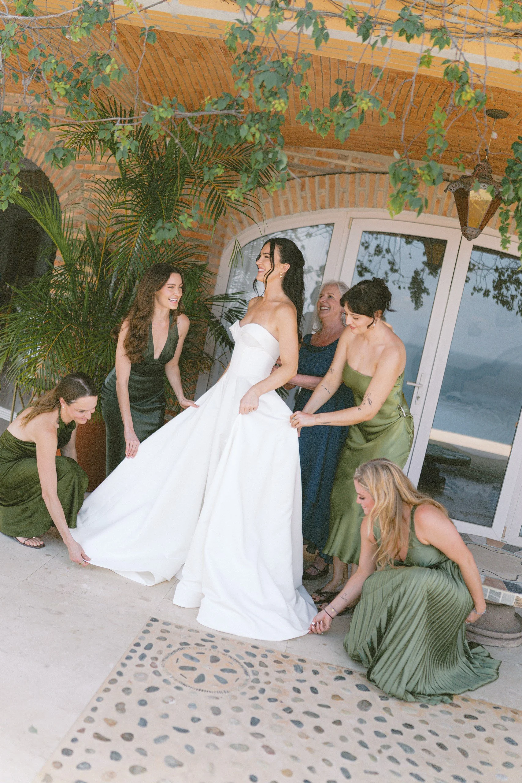 Bridesmaids in green dresses helping the bride with her gown before the wedding at Gran Villa, Sayulita