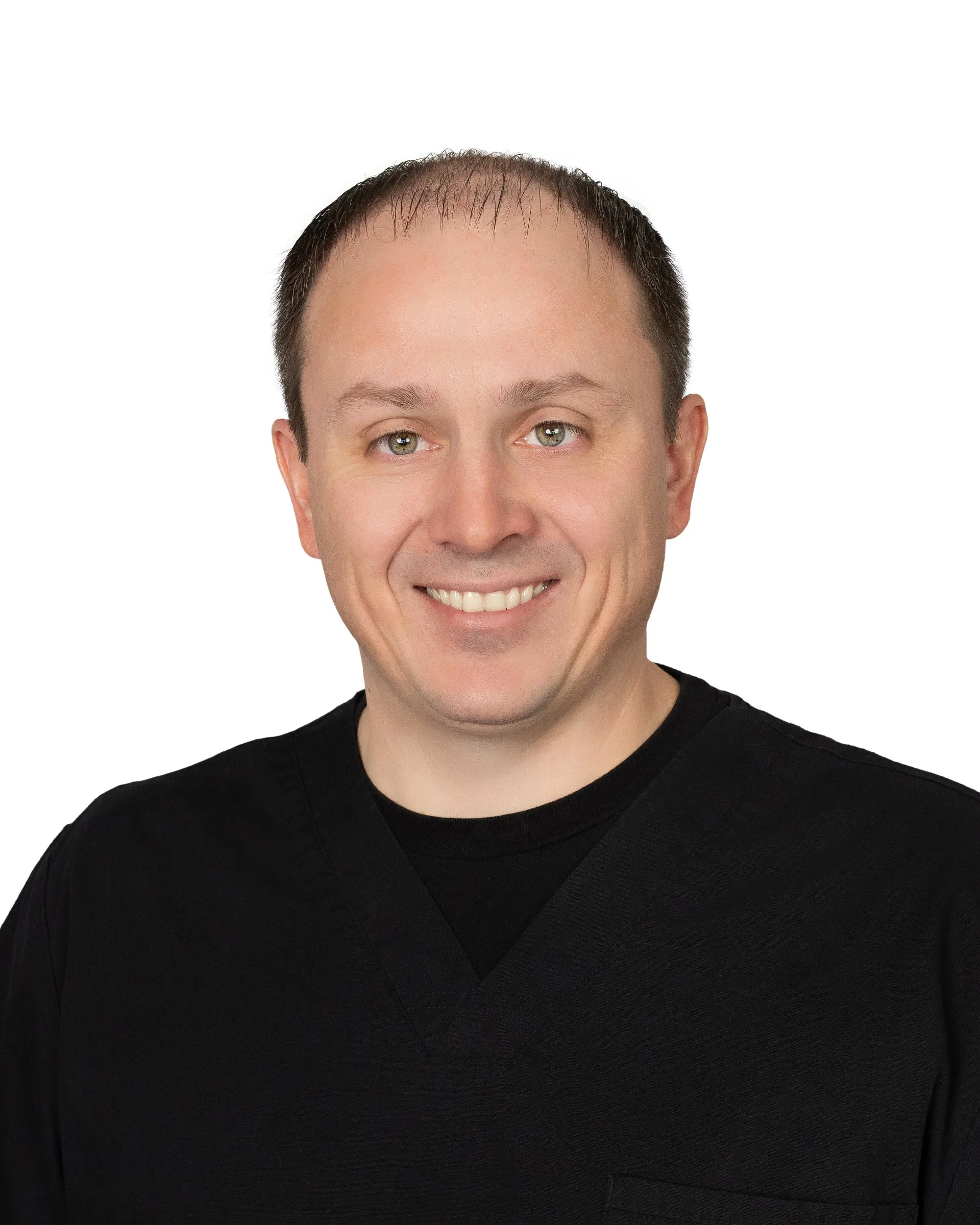 Portrait of a smiling man with short, dark hair wearing black medical scrubs against a white background.