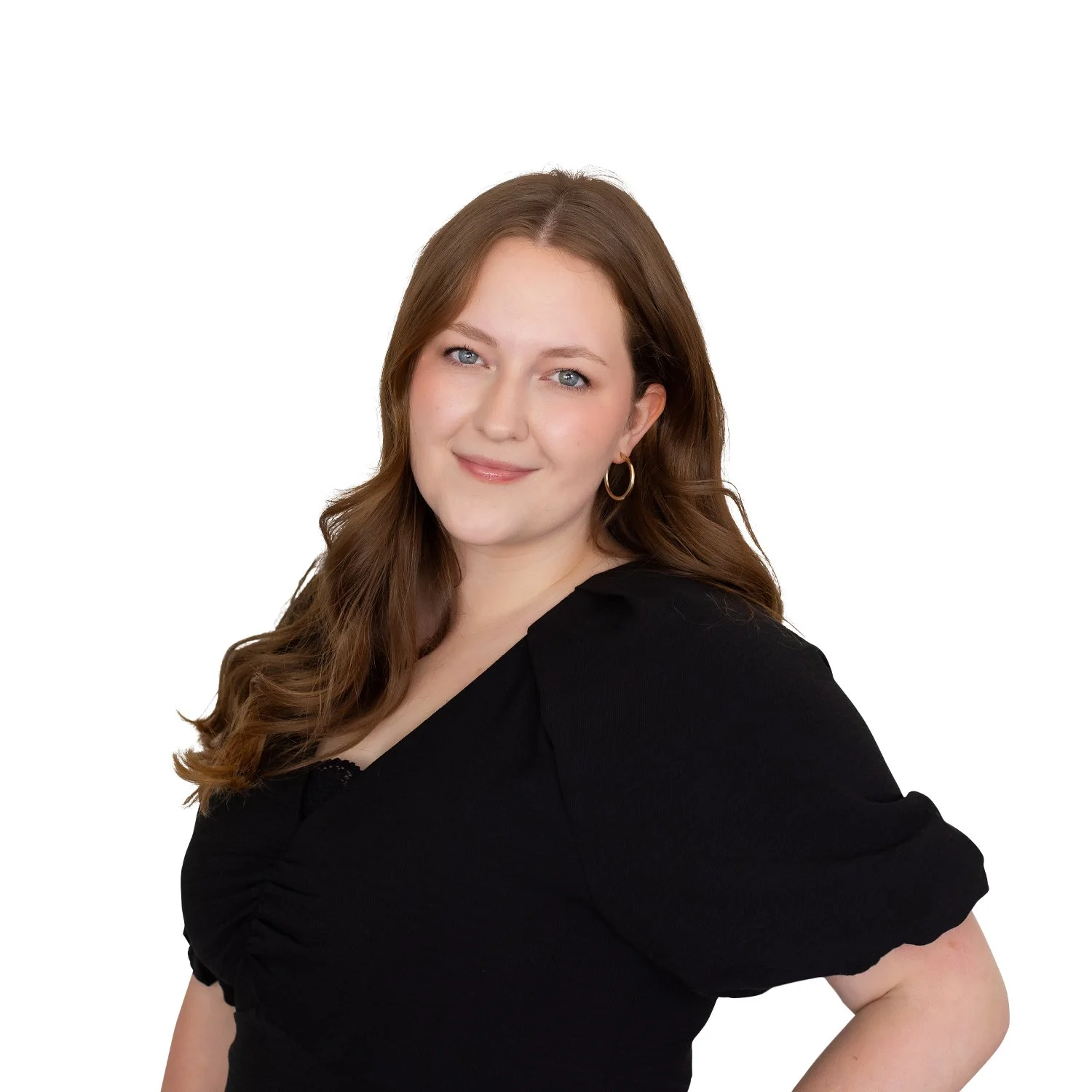 Portrait of a woman with long brown hair, blue eyes, and fair skin, wearing a black top and gold hoop earrings, smiling against a white background.
