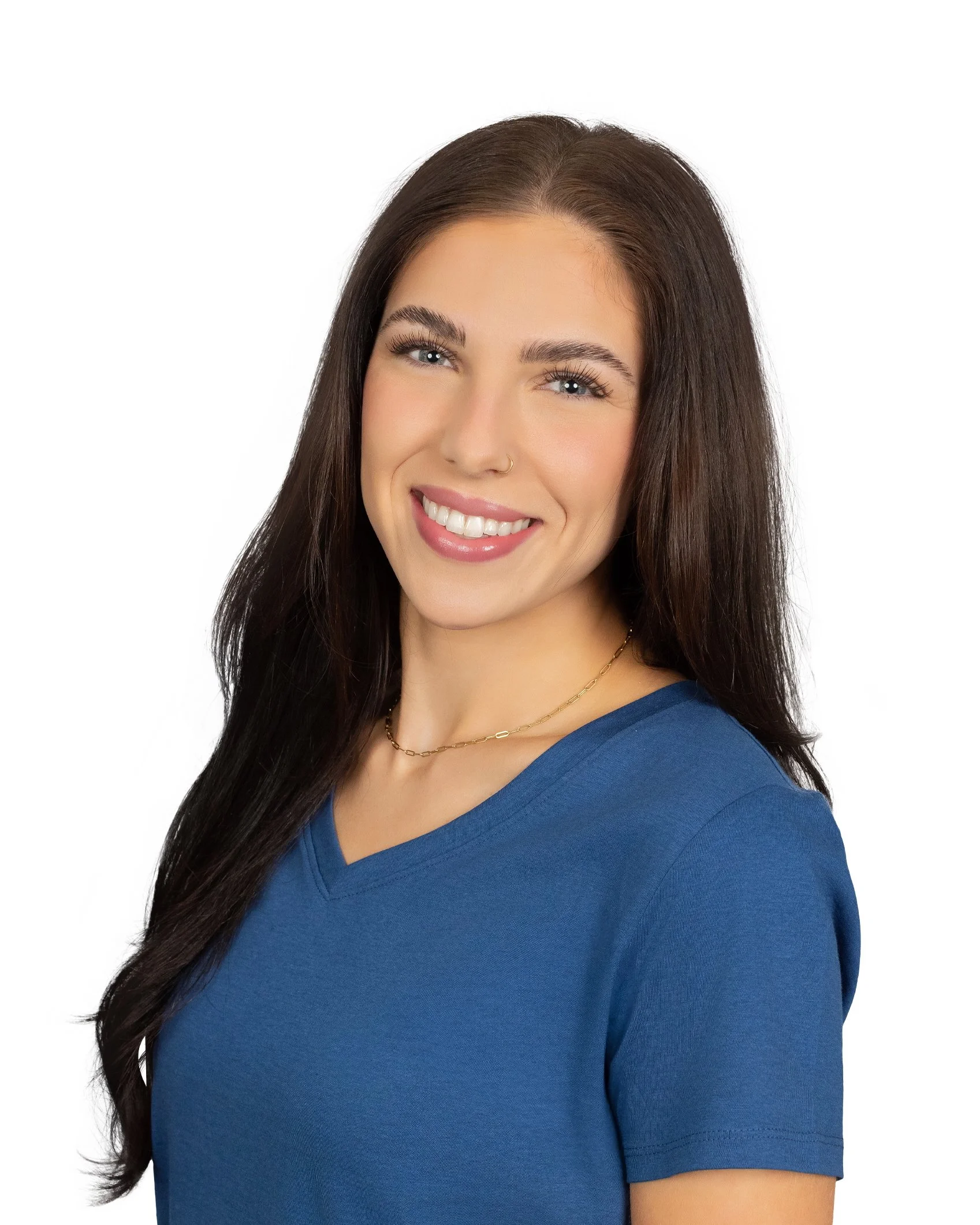A woman with long dark brown hair, light skin, wearing a blue V-neck shirt, smiling, against a white background.