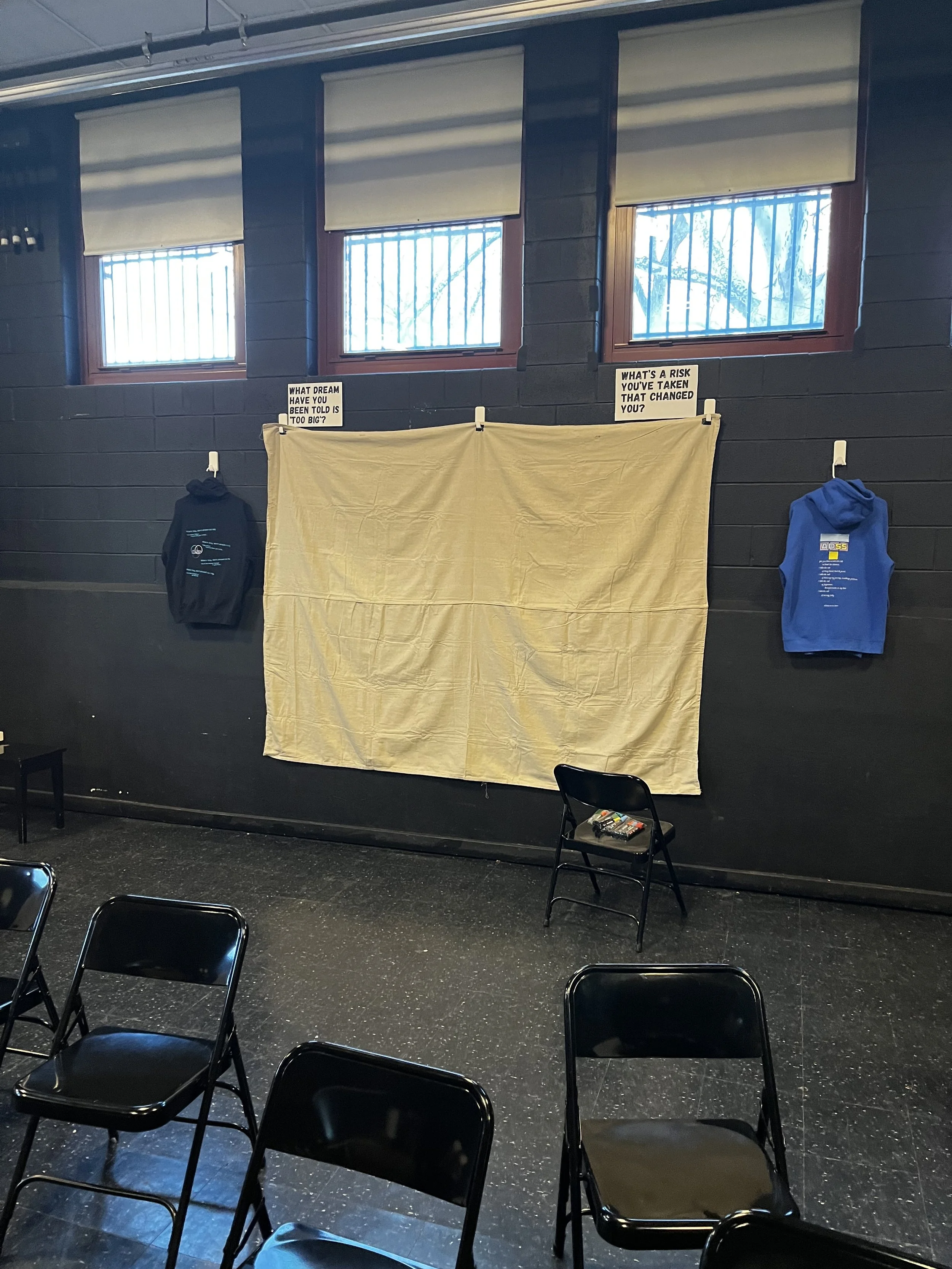 Textual Tapestry hanging from wall with two ADSS poem hoodies beside it